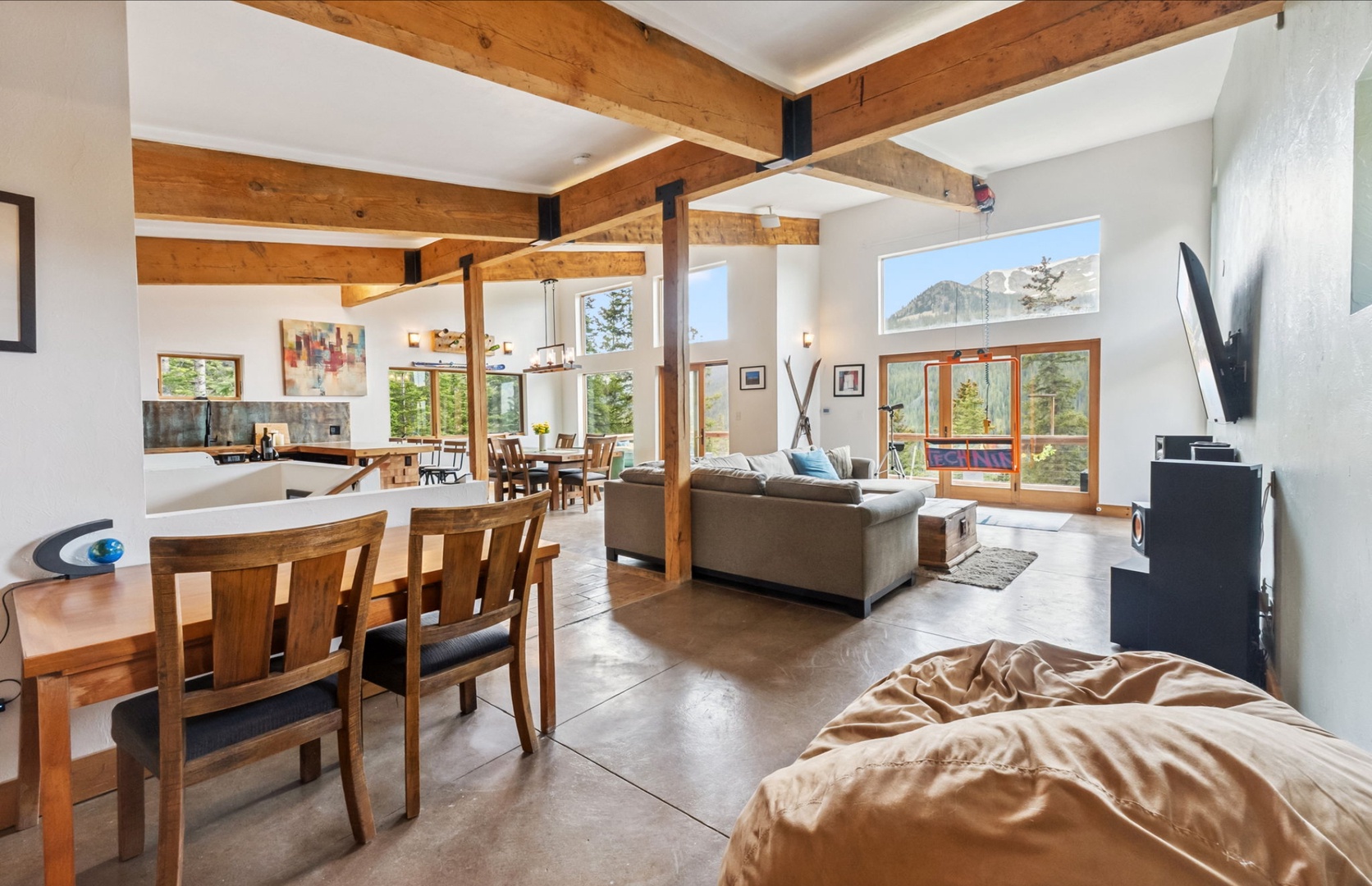 Soaring beams frame your mountain retreat where natural light pours through expansive windows, bringing alpine views into your open living and dining space. Relax on plush seating and savor meals surrounded by rustic warmth.