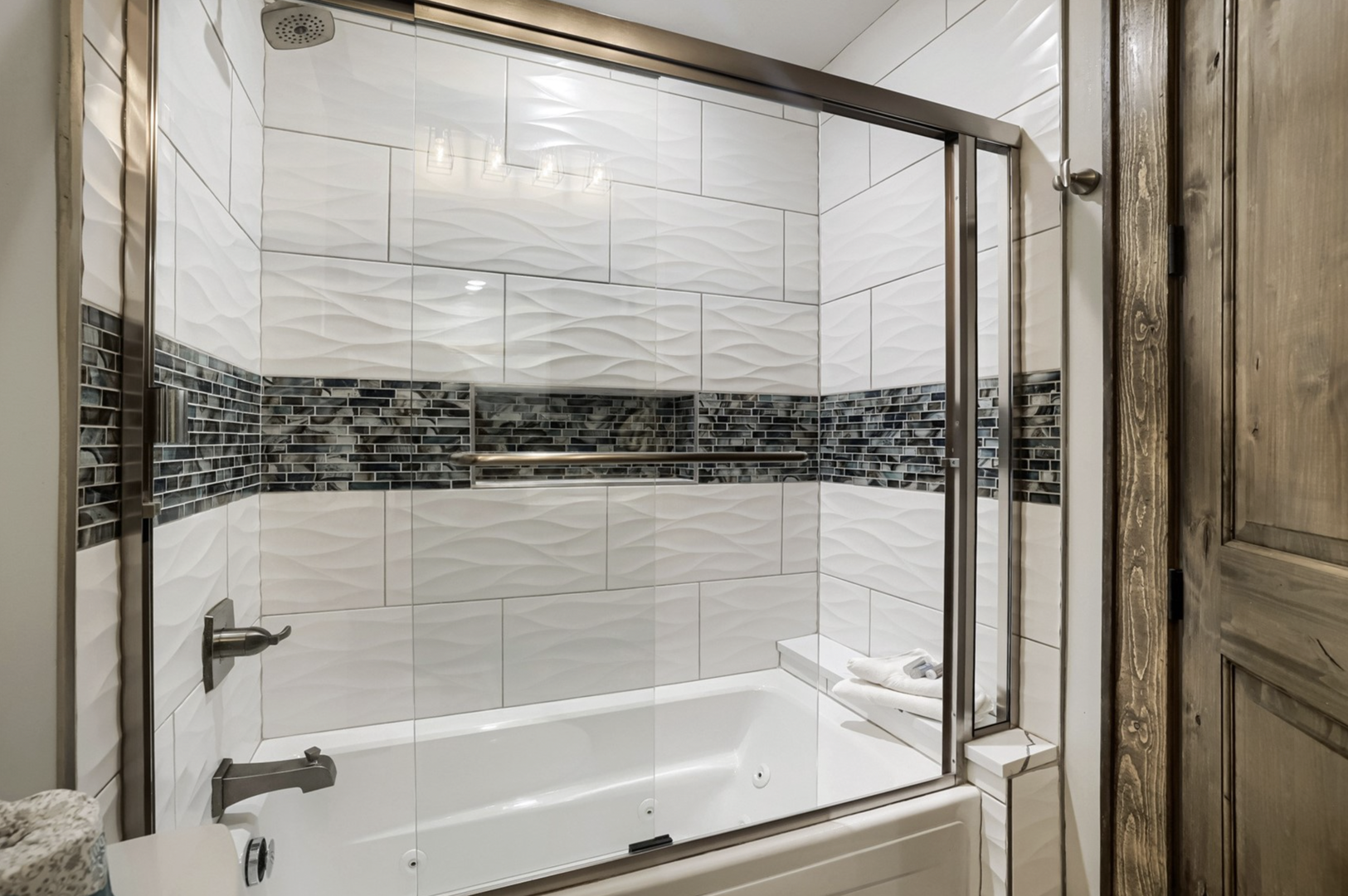 Step into your beautifully tiled bathroom, where a modern glass-enclosed tub and shower await. Striking wave-textured white tiles and sleek gray accents create a refined, spa-like retreat just for you.