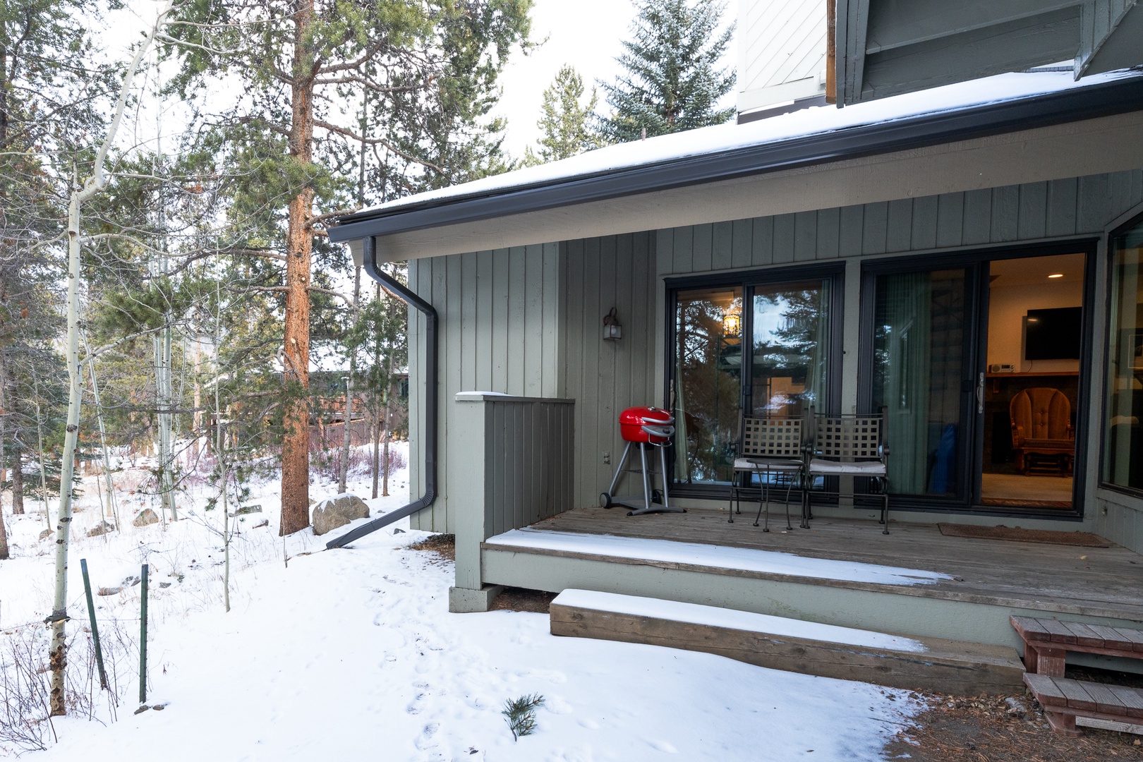 Modern mountain retreat nestled among snow-dusted pines, featuring a covered deck with BBQ and outdoor seating perfect for year-round relaxation.