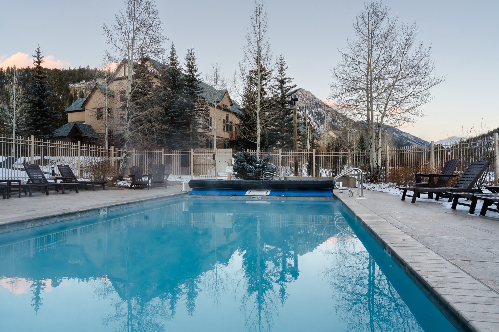 Winter mountain resort featuring an outdoor heated pool surrounded by snow-covered peaks and alpine forest scenery.