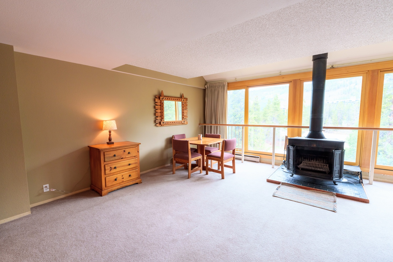 Cozy up by the wood-burning stove while gazing through expansive windows framing lush mountain views, perfect for peaceful mornings or quiet evenings in your retreat.