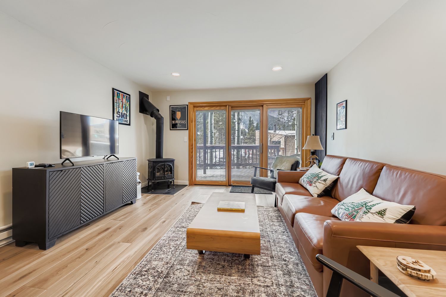 Relax in your cozy living room featuring warm leather seating, a classic fireplace, and large windows opening to your private balcony with mountain views.