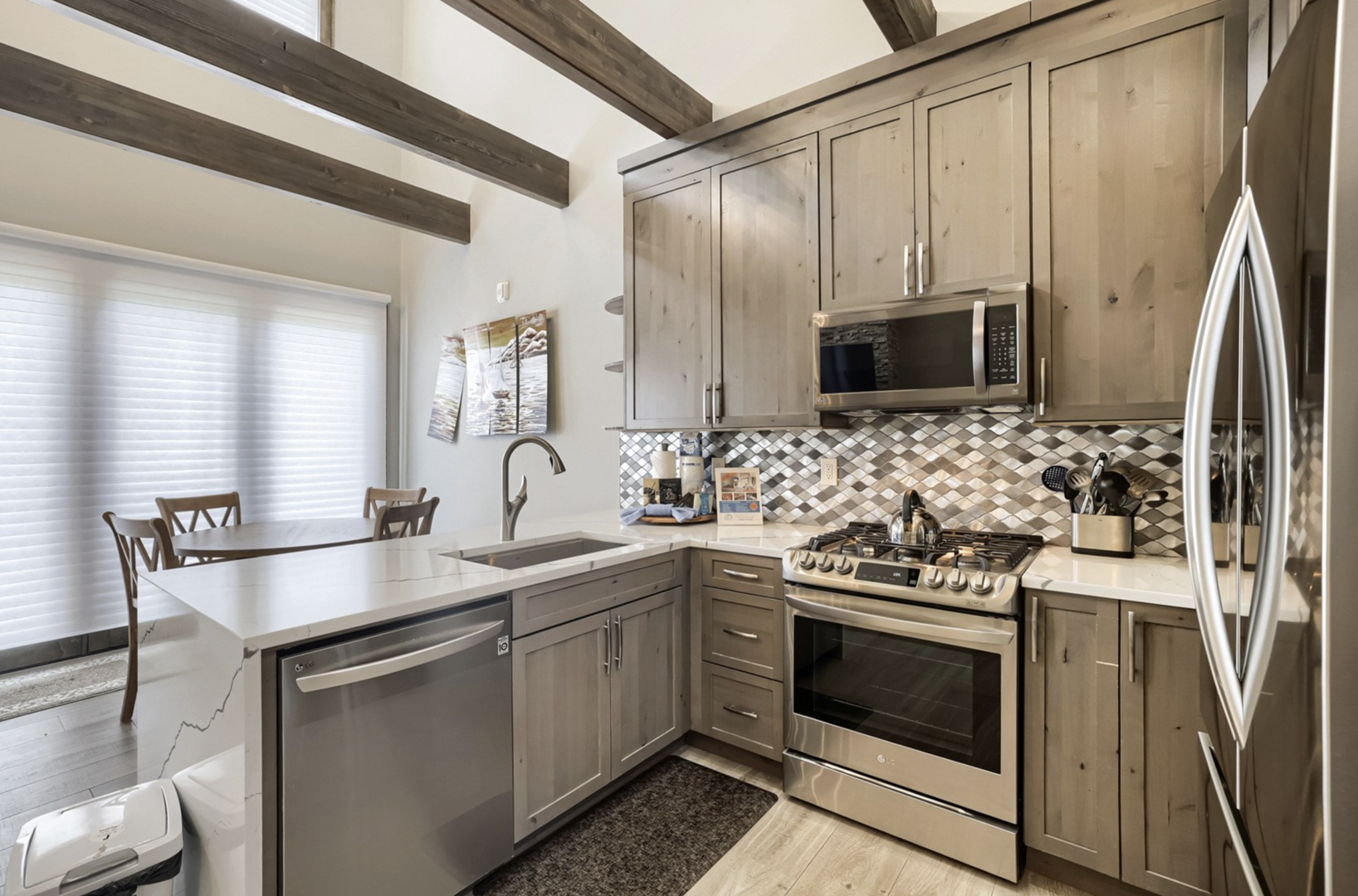 Your well-appointed kitchen features sleek stainless steel appliances, elegant stone countertops, and a charming mosaic backsplash, all beneath rustic exposed beam ceilings that add warmth and character to your culinary space.