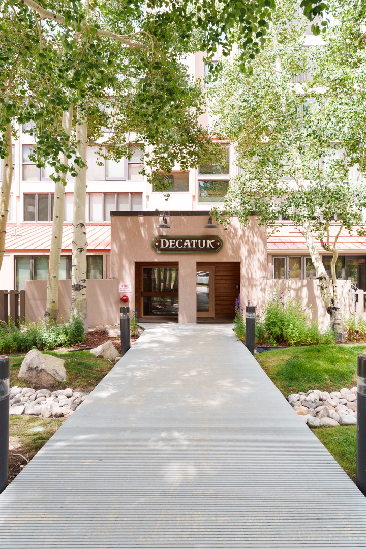 The property entrance features a welcoming walkway framed by mature trees and thoughtfully landscaped gardens, marked by the Decatur sign above the front door.