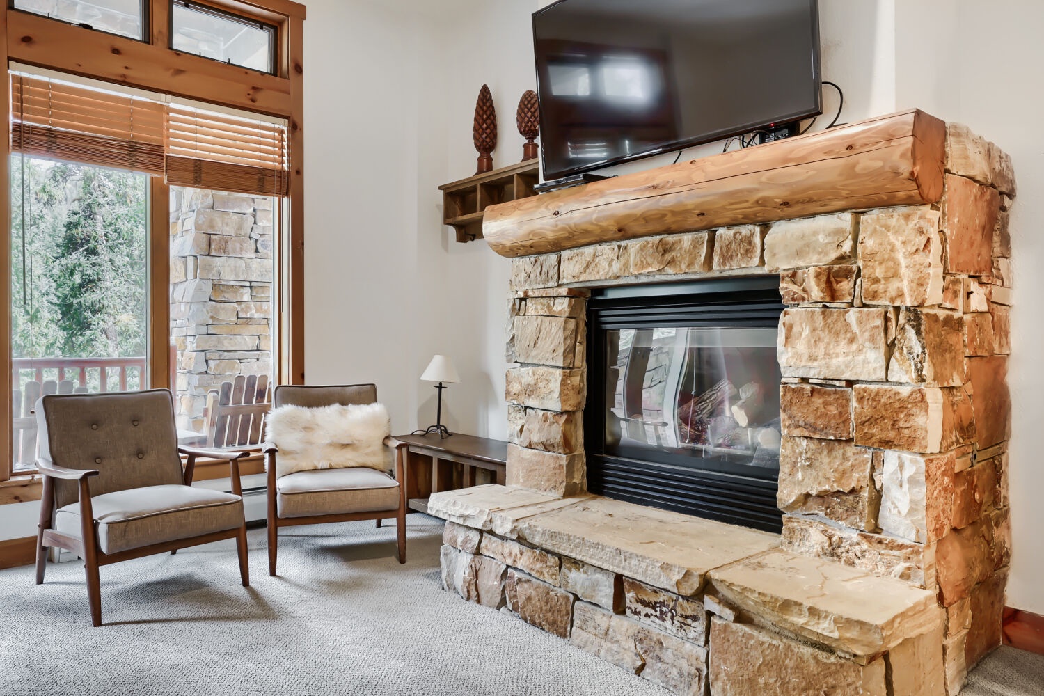 Curl up in your cozy living room, where a rustic stone fireplace with reclaimed wood mantel anchors the space. Natural light pours in through tall windows framing peaceful forest views, perfect for unwinding after a day of adventure.