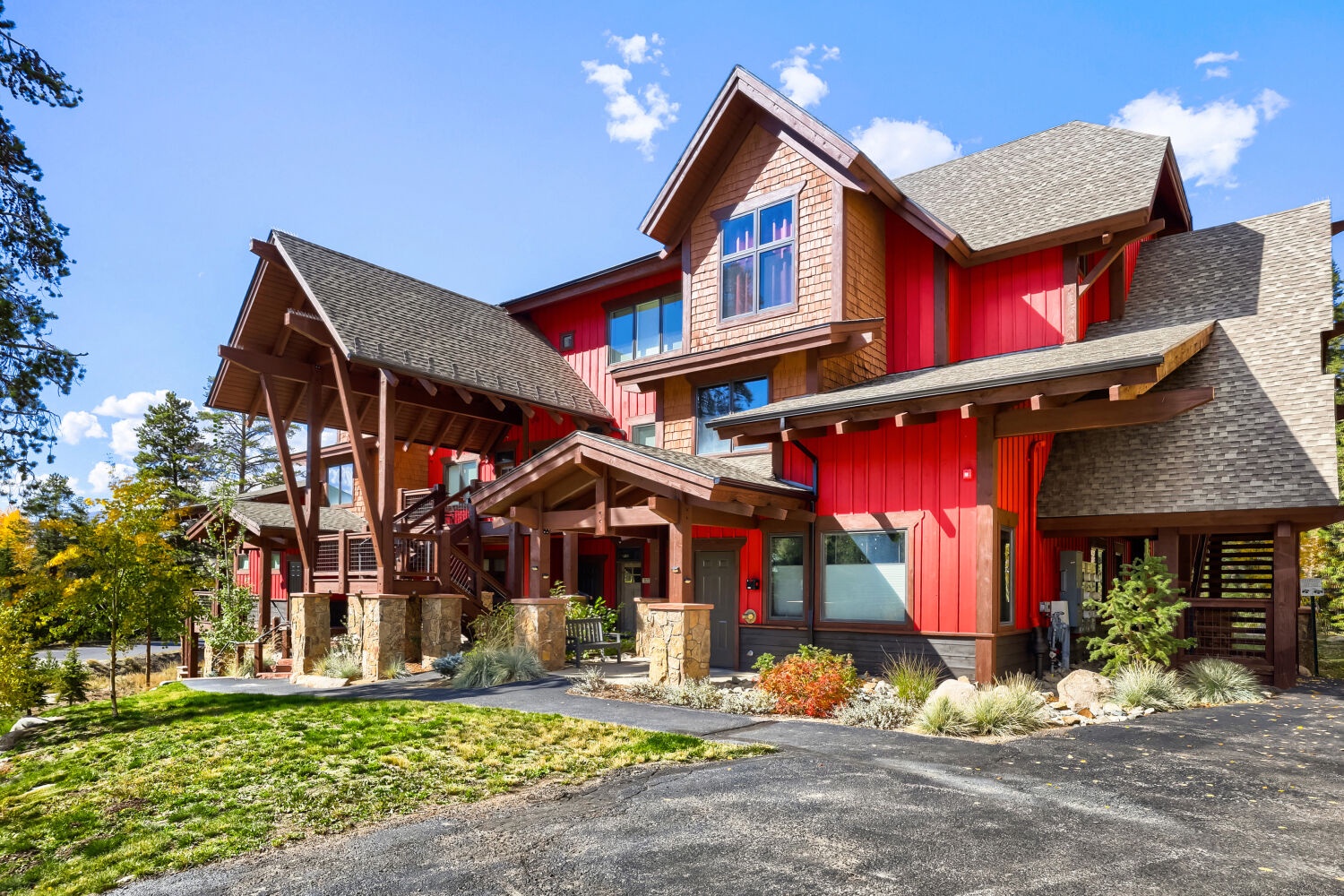 Striking mountain lodge architecture featuring bold red siding, natural wood accents, and stone pillars set against a pristine alpine backdrop—a distinctive property welcoming you to your mountain getaway.