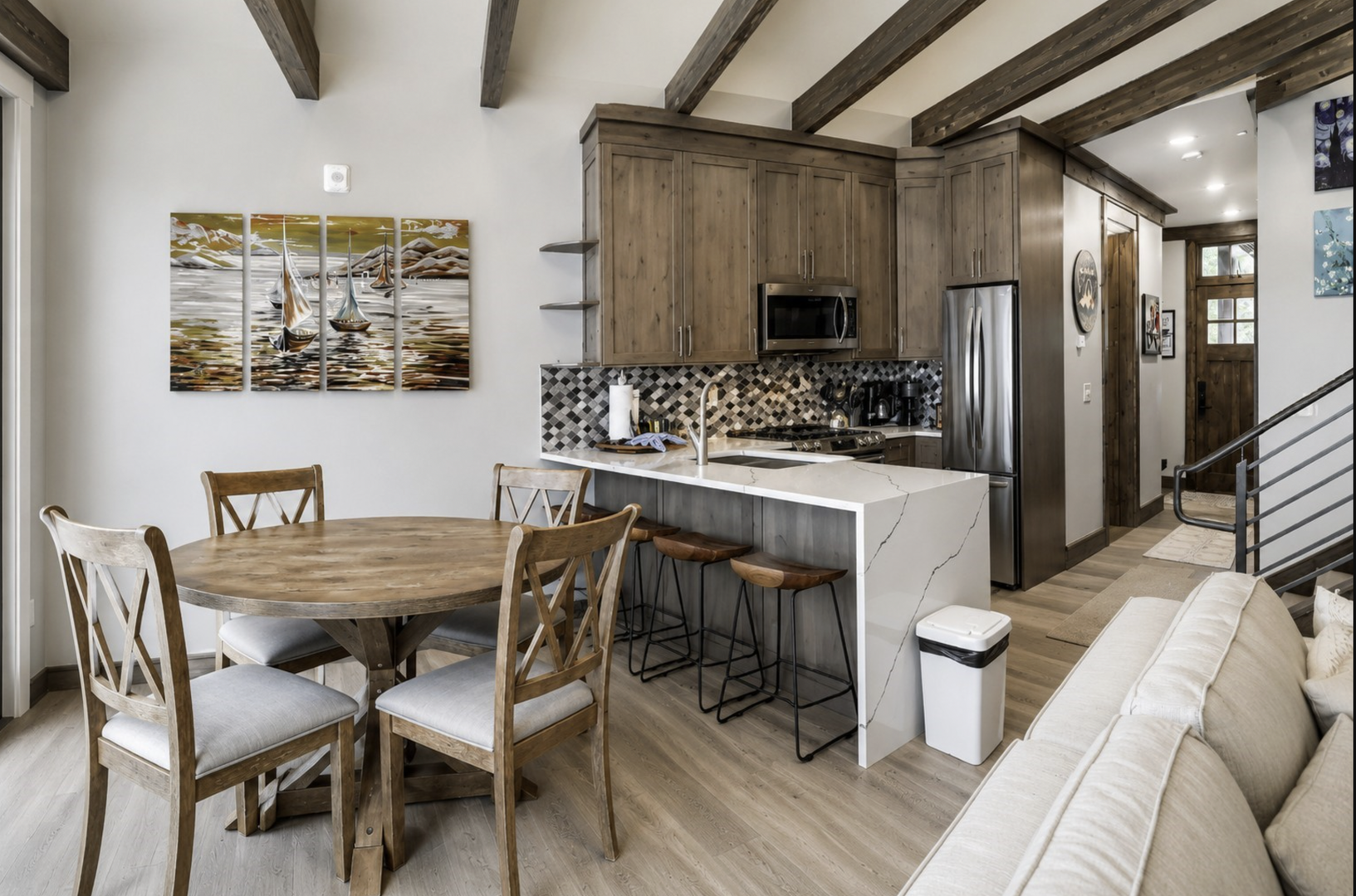 Settle into your open-concept living space where rustic wood beams meet modern comfort. Cook in the stylish kitchen, gather around the dining table, and relax on the inviting sofa—all under one beautiful vaulted ceiling.