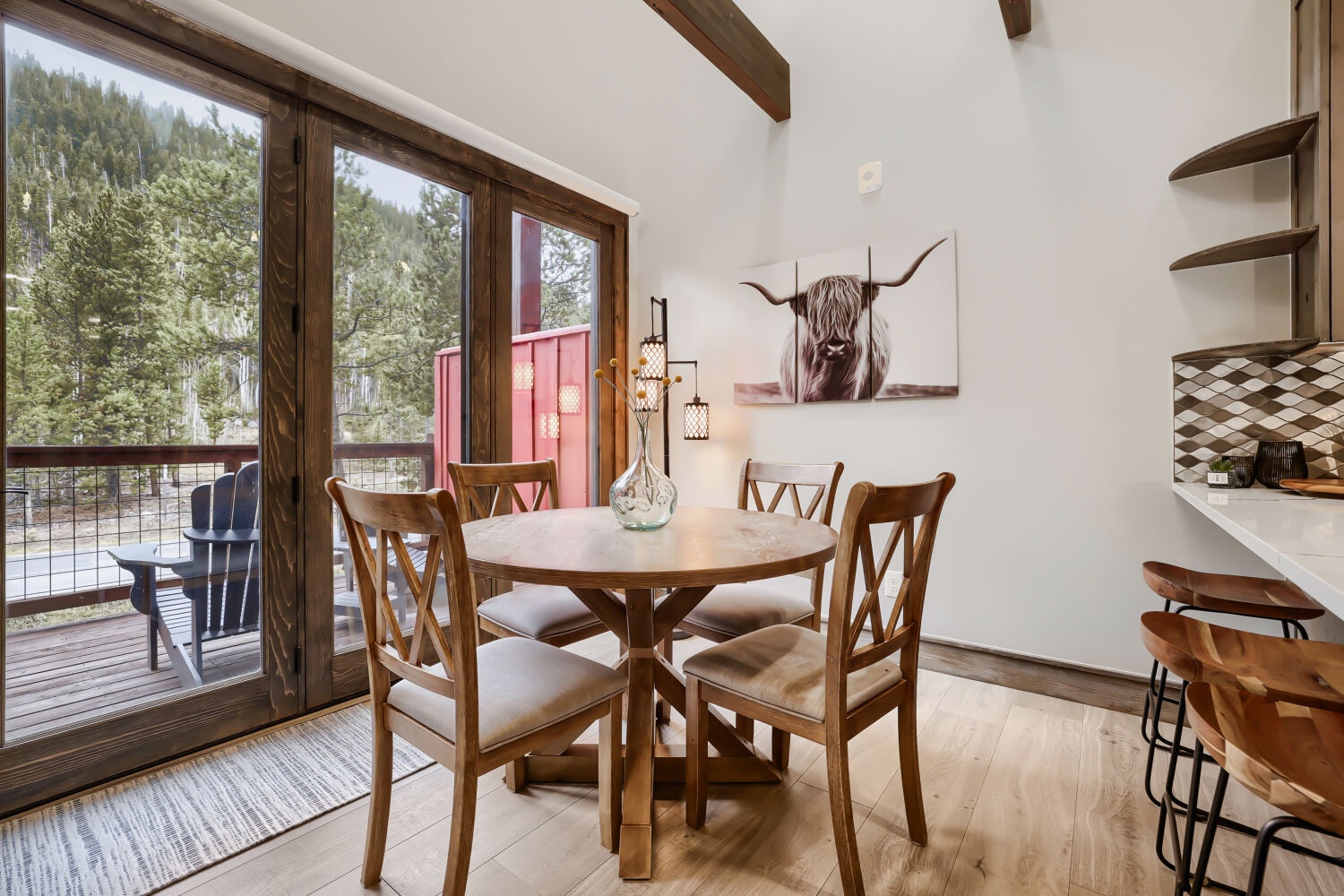 Step into your bright dining space where rustic wood beams frame expansive forest views through floor-to-ceiling windows. Gather around the warm wooden table for morning coffee or evening meals with nature as your backdrop.