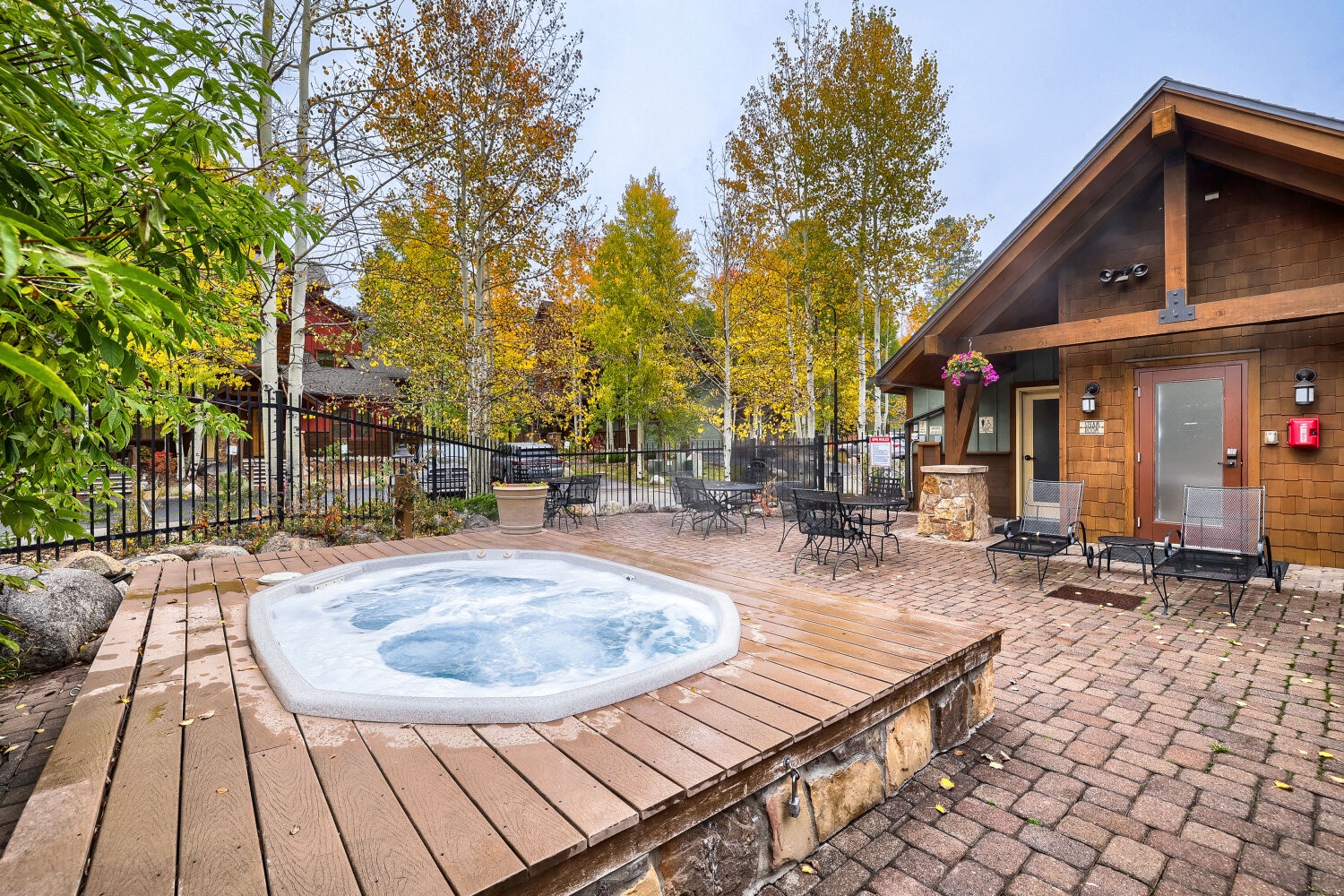 A communal hot tub set on a wooden deck surrounded by autumn foliage and outdoor seating, offering a peaceful spot to unwind after your mountain adventures.