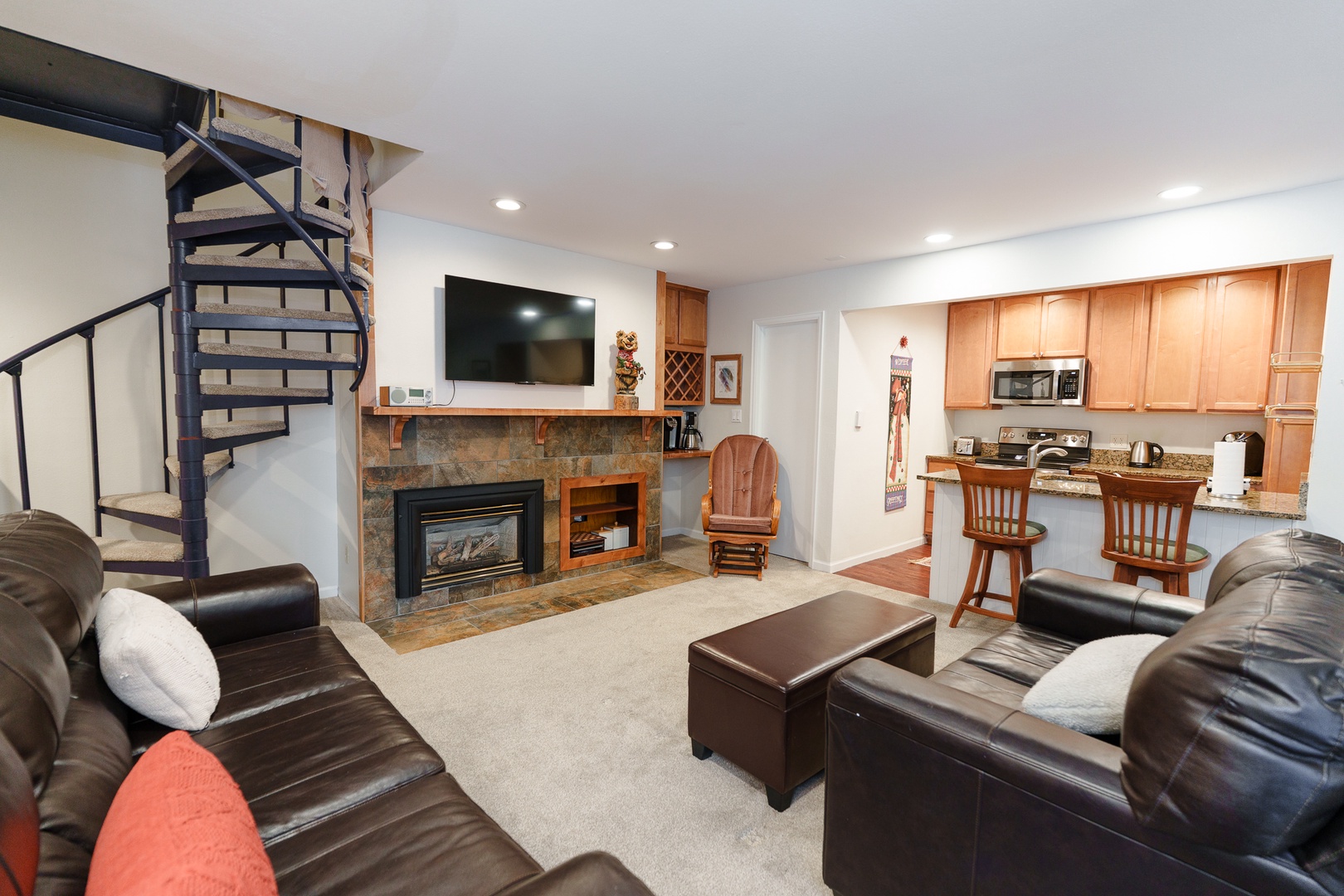 Relax in your spacious living area featuring comfortable leather seating, a cozy stone fireplace, and open kitchen perfect for gathering with friends and family.
