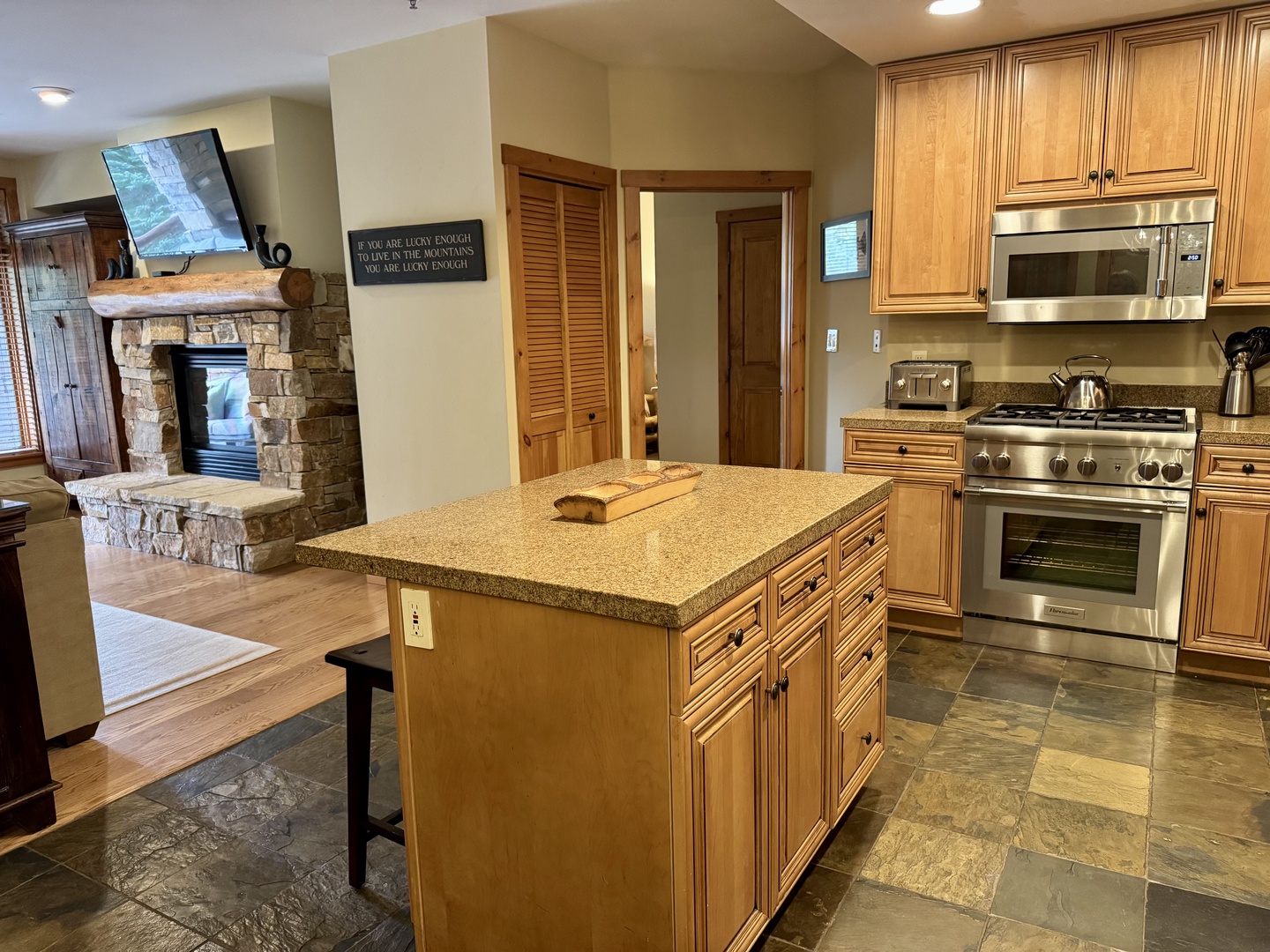 Your mountain retreat's kitchen invites you to gather and create, with a granite island at its heart, stainless steel appliances ready for your use, and a cozy stone fireplace adding warmth to every meal.