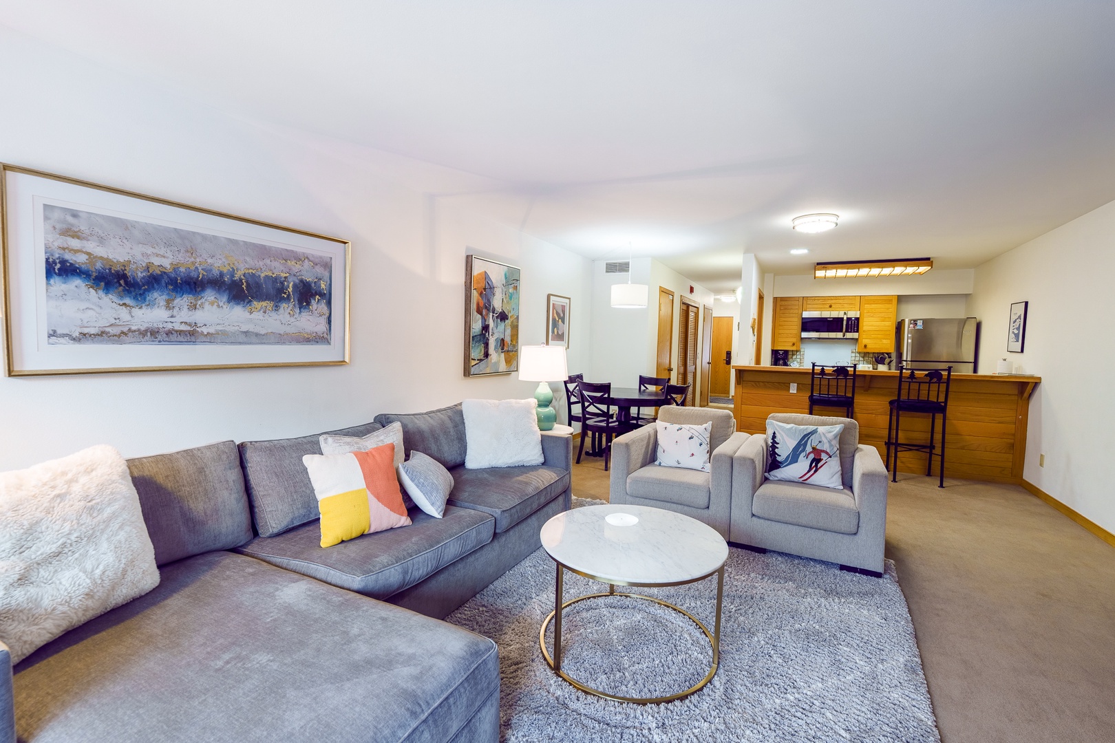 Sink into plush gray seating with colorful pillows while you enjoy your open-concept living space with kitchen and dining area.