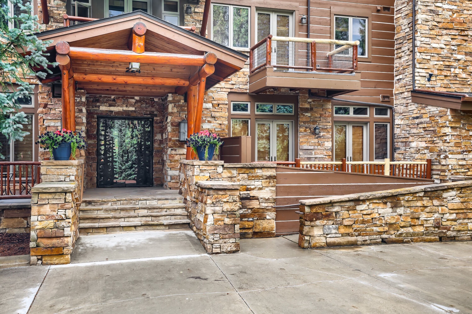 The lodge-style entrance features warm timber beams and stacked stone pillars with colorful planters welcoming guests to the property.