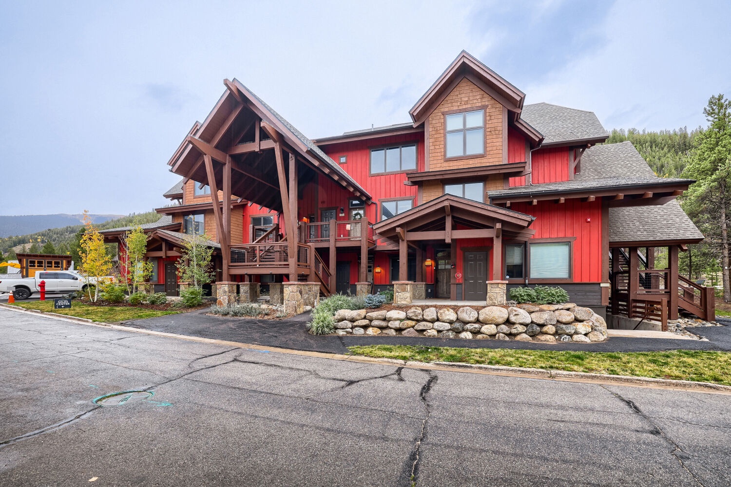 A striking red mountain lodge with timber accents and stone landscaping, located near forested hillsides.