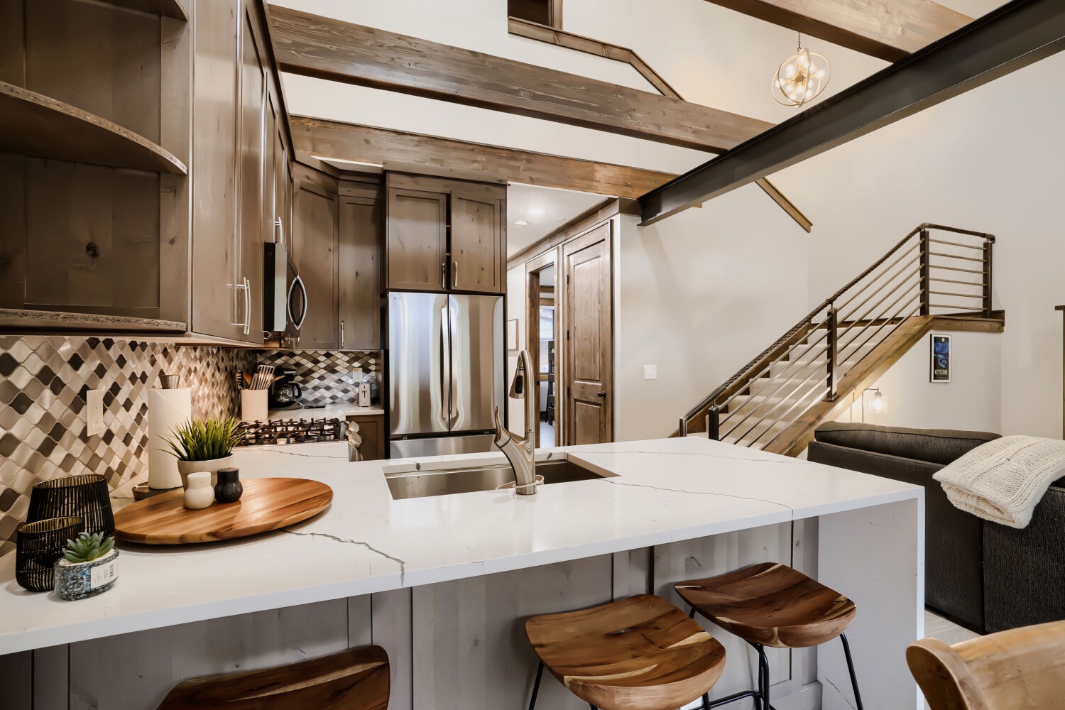 Gather around your sleek kitchen island where rustic warmth meets modern design—exposed beams overhead, soaring ceilings, and a cozy living space just steps away invite you to make yourself at home.