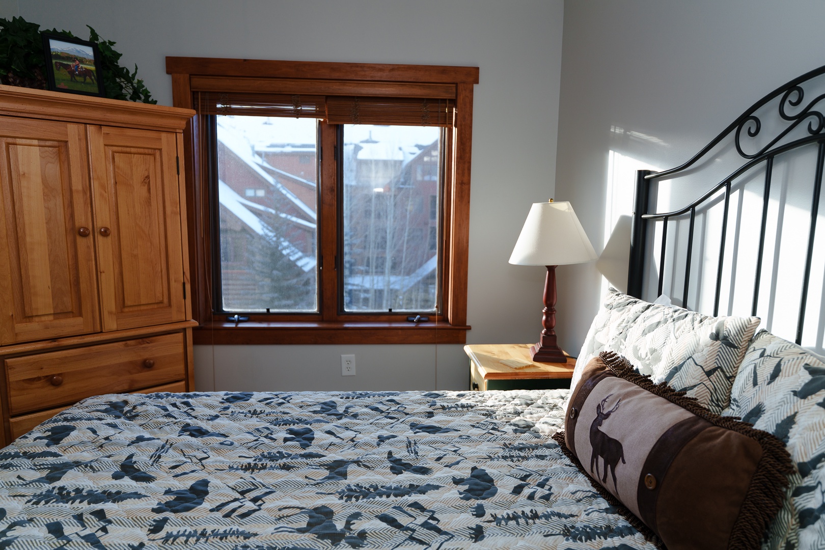 Your cozy bedroom features rustic wood furnishings and mountain lodge-style bedding, with a window showcasing the surrounding alpine landscape.