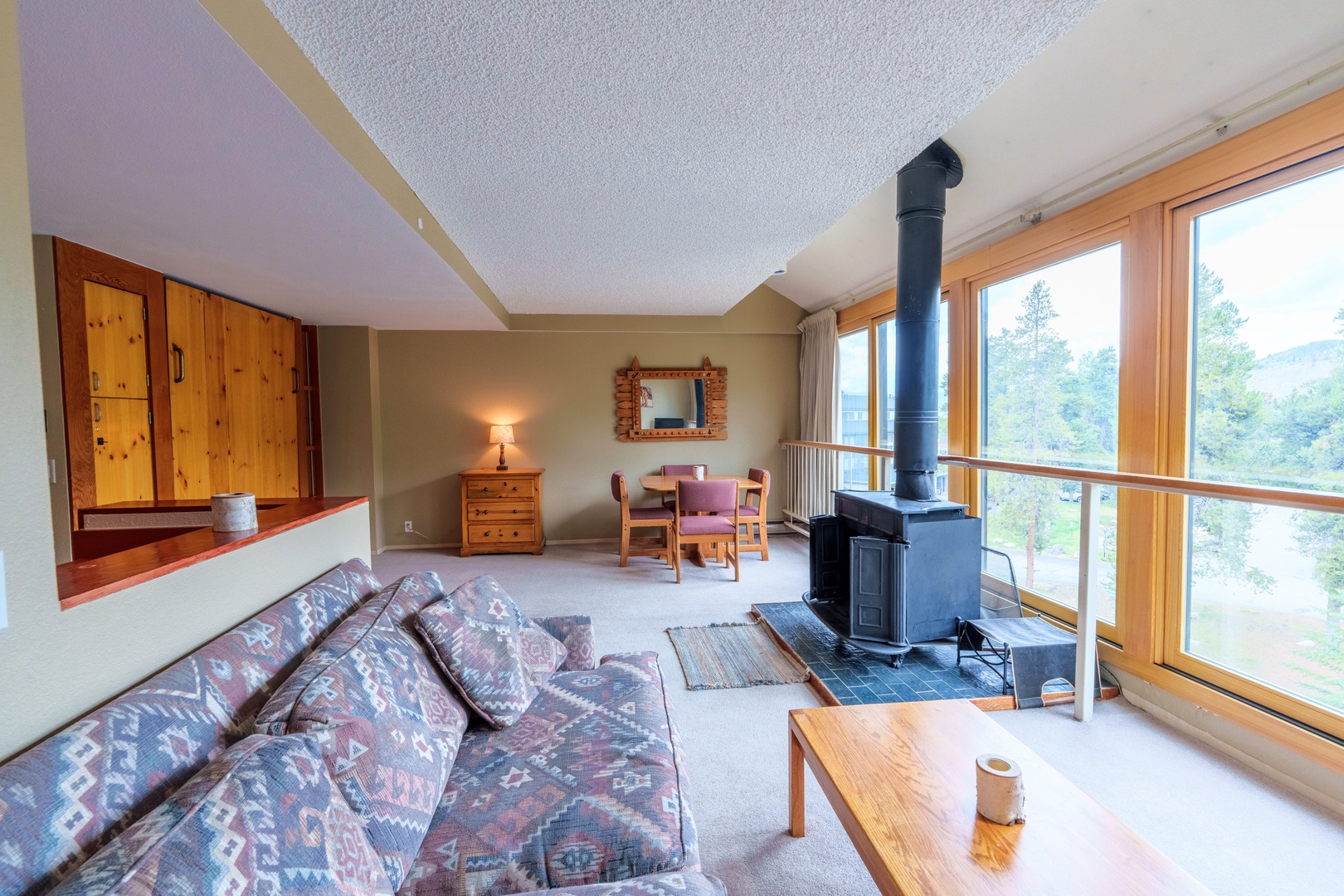 Your cozy alpine retreat features a wood-burning fireplace and expansive windows framing stunning mountain views. Warm wood tones and comfortable furnishings create a welcoming space to unwind after exploring the outdoors.