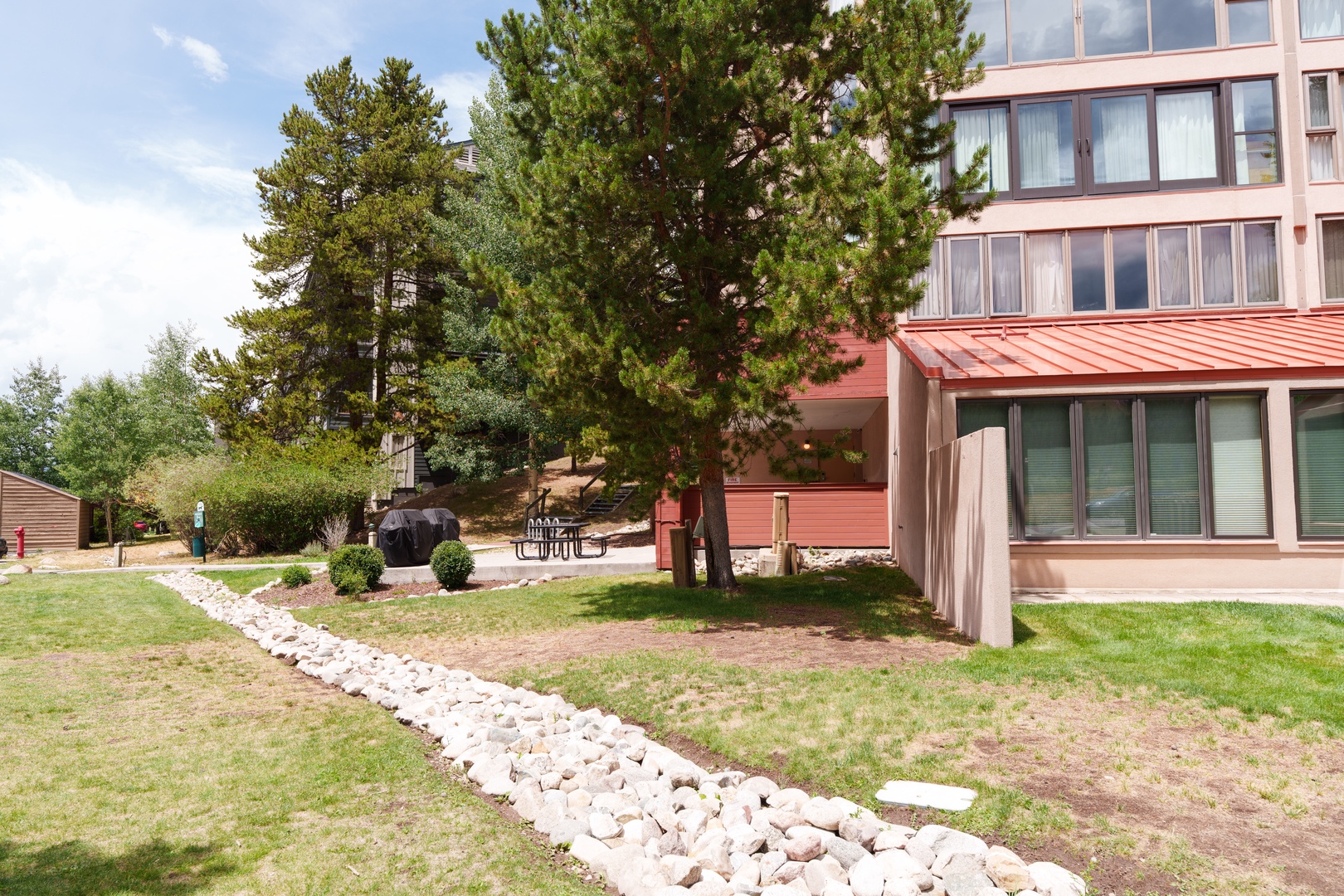 The property sits nestled among mature pines and landscaped grounds, with outdoor seating and a BBQ area ready for leisurely afternoons in the fresh mountain air.