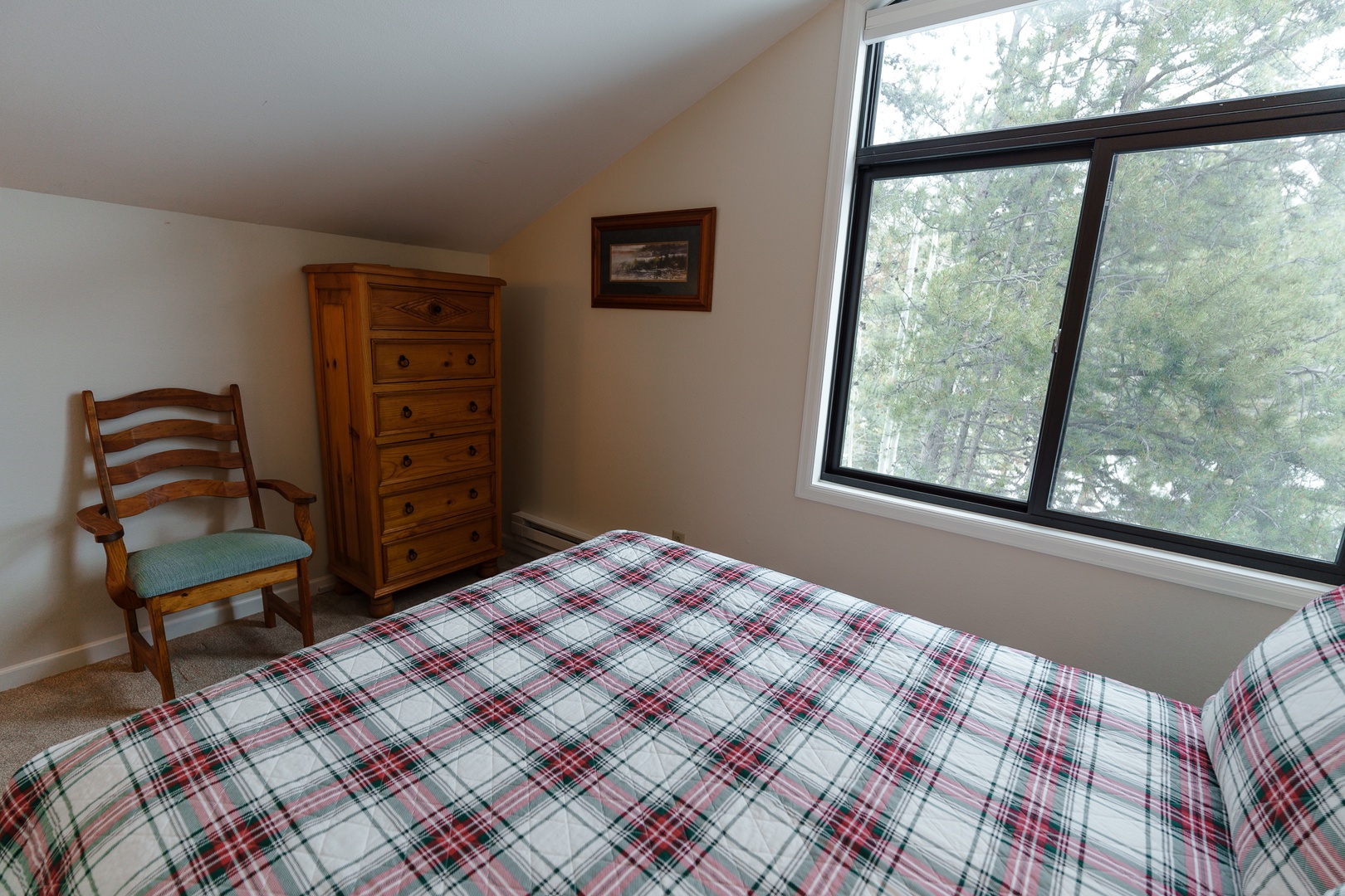 Wake up to peaceful tree views from your cozy bedroom featuring classic wooden furniture and comfortable seating for a restful mountain retreat.