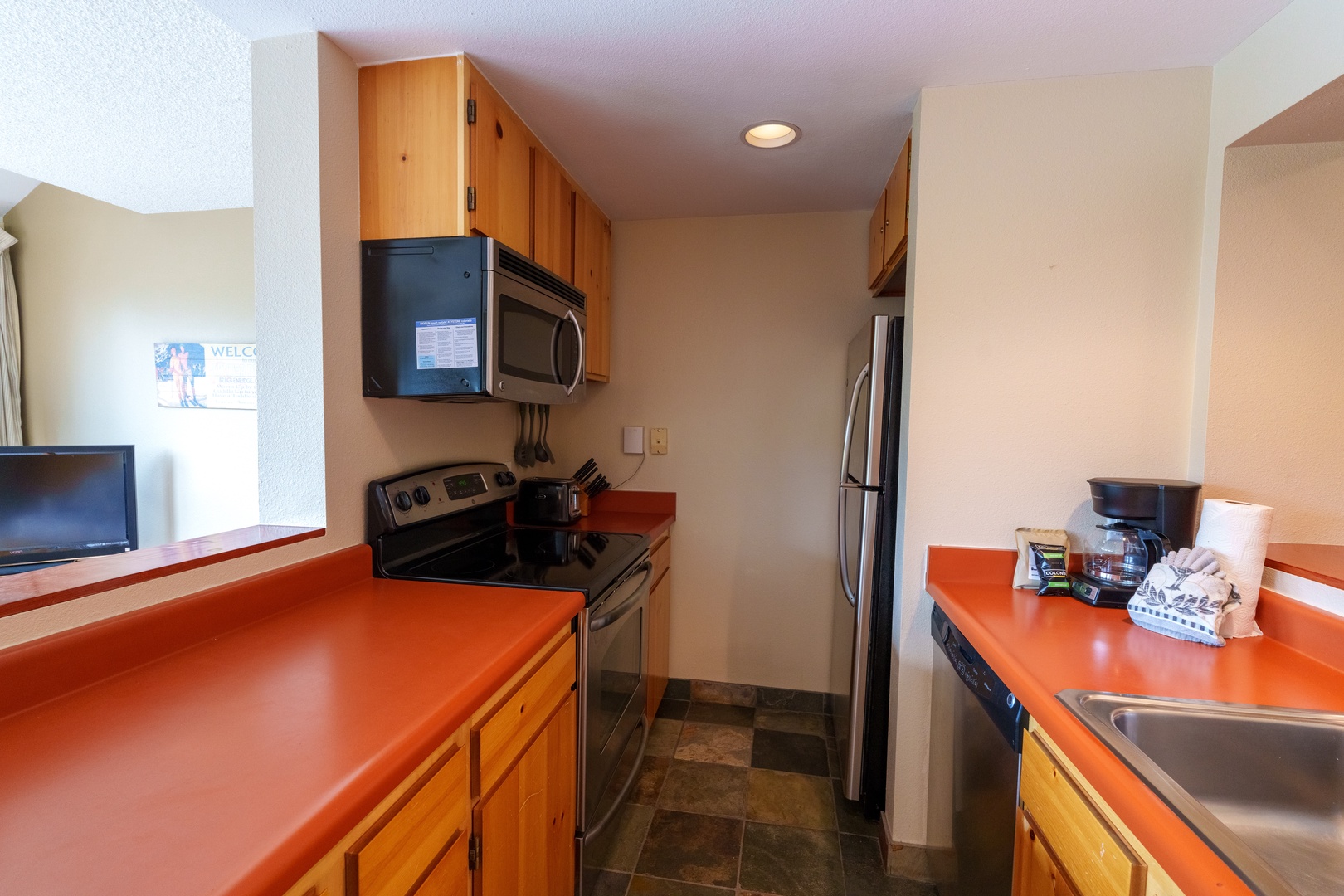 Your fully equipped galley kitchen has everything you need—stainless appliances, bold orange countertops, and all the essentials for preparing meals at your leisure.