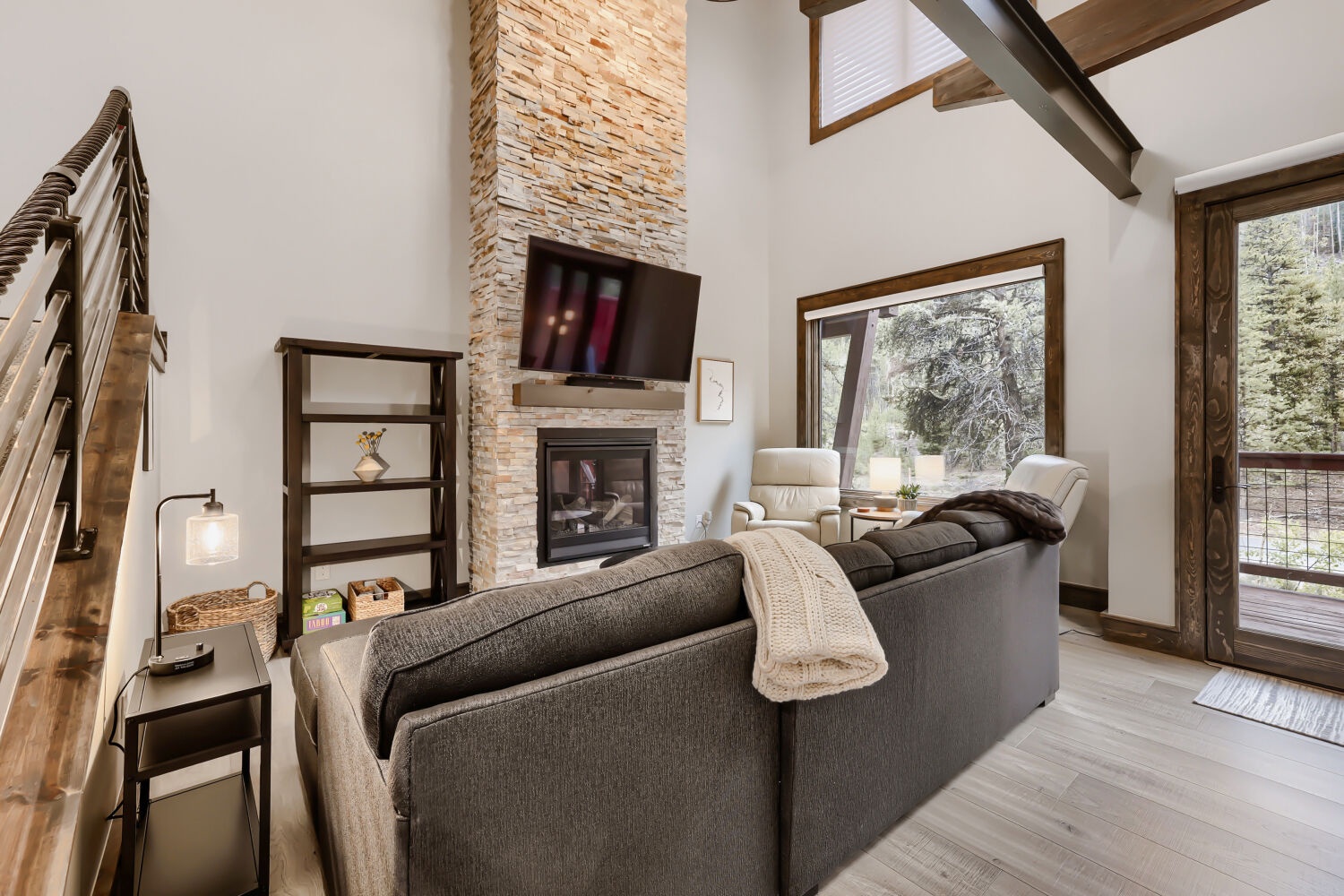 Unwind in your bright, open living room with soaring ceilings, a warm stone fireplace, and natural light streaming through tall windows. Cozy up here after a day exploring the mountains.