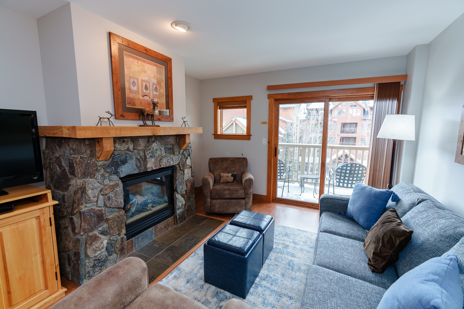 Unwind in your cozy living room featuring a stone fireplace, comfortable seating, and private balcony access with mountain views.