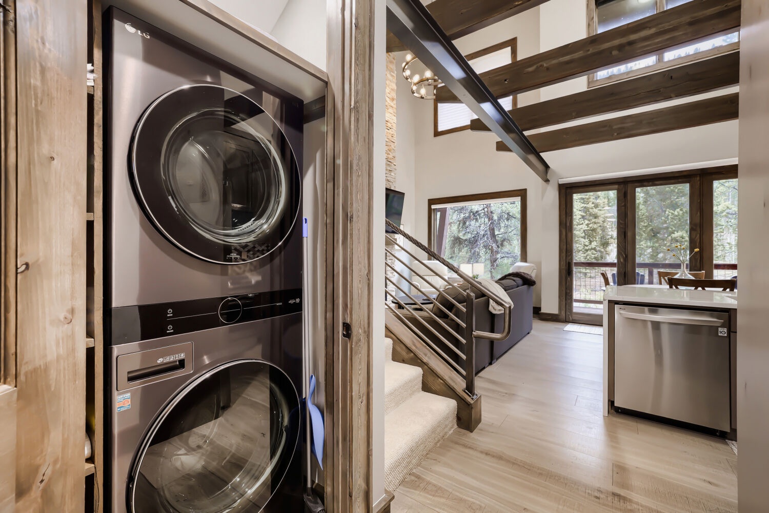 Your laundry stays effortless with stacked washer and dryer tucked neatly within reach, while natural light pours through the vaulted living space beyond.
