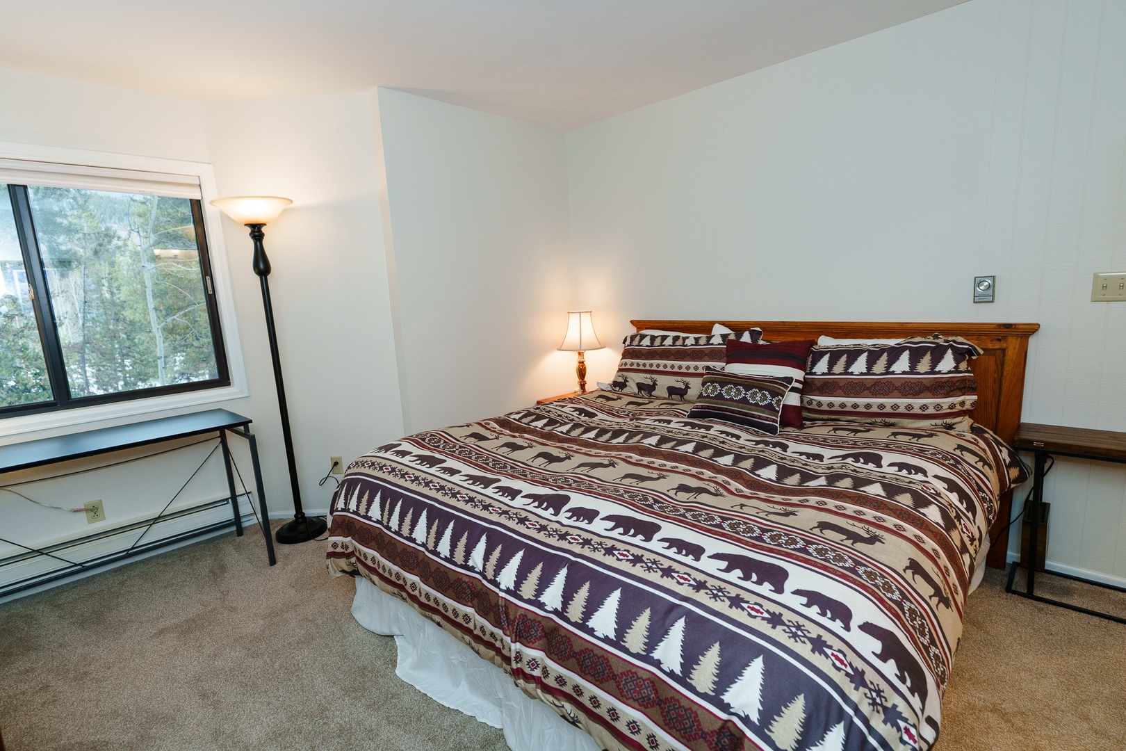 Your cozy primary bedroom features a comfortable queen bed with rustic mountain-themed bedding, peaceful forest views, and warm lighting to help you unwind after a day of adventure.