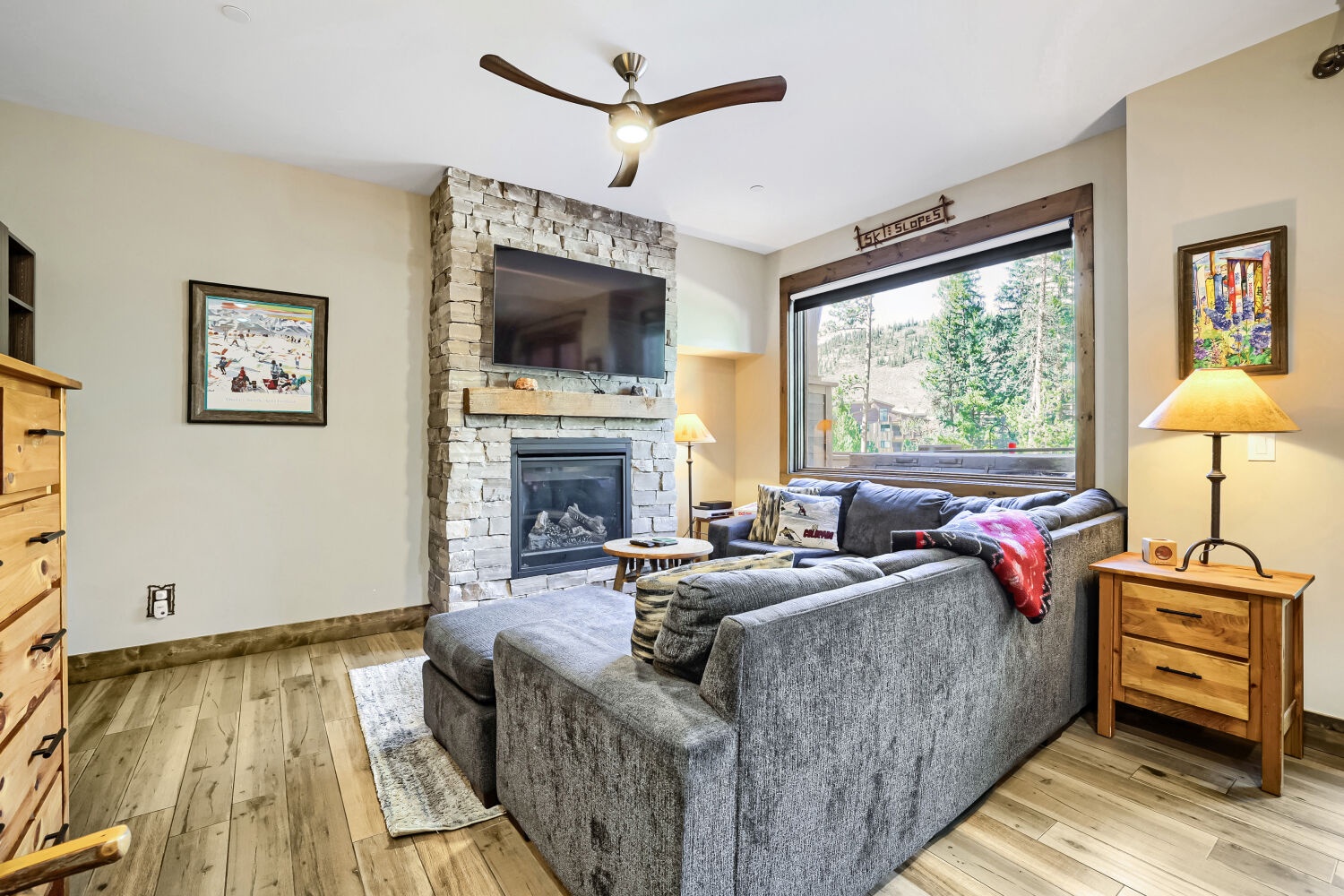 Curl up on the plush sectional by the fireplace as natural light streams through the large window, revealing peaceful wooded views perfect for your mountain escape.
