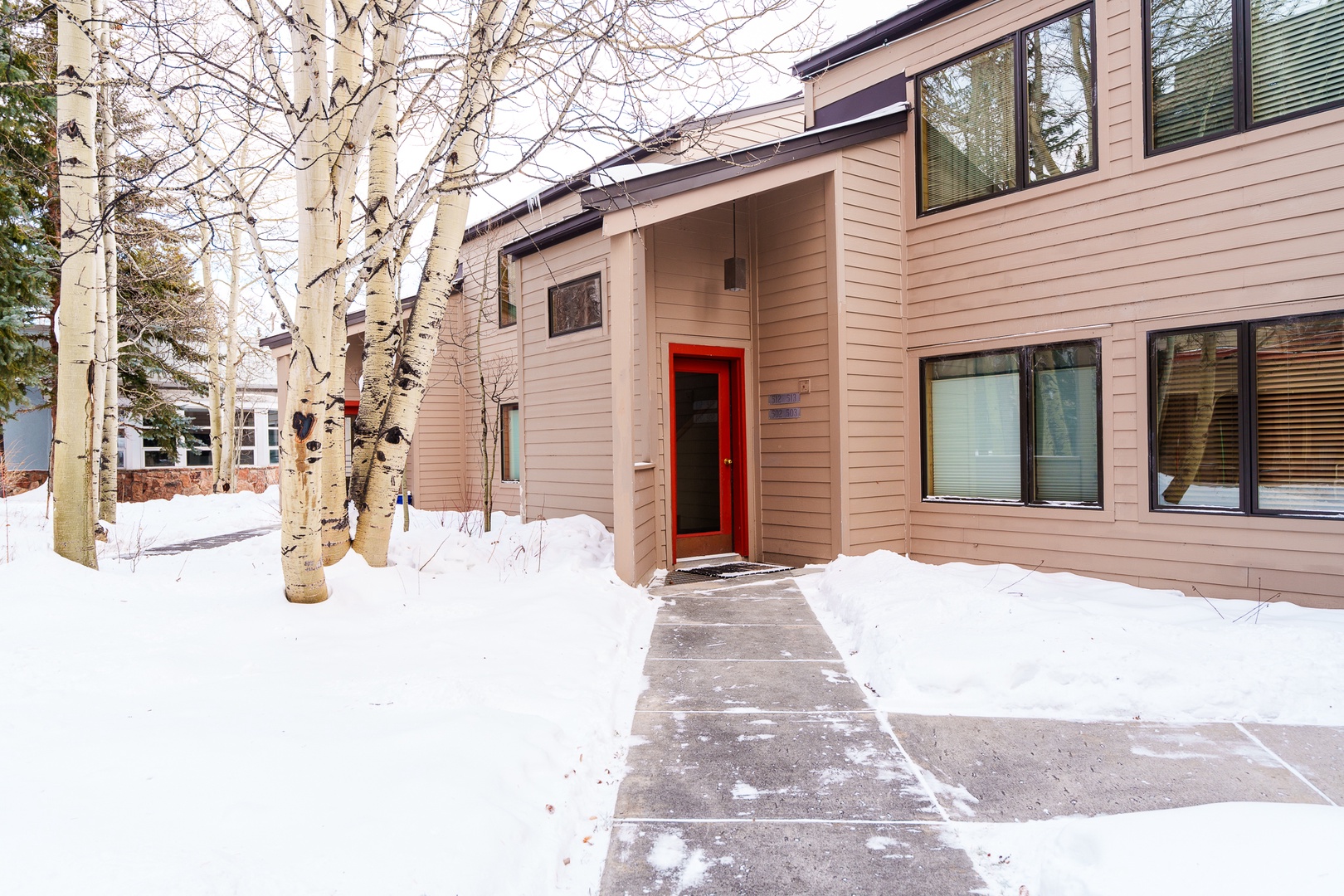 A welcoming mountain retreat with distinctive red entrance door surrounded by snow-covered aspens.