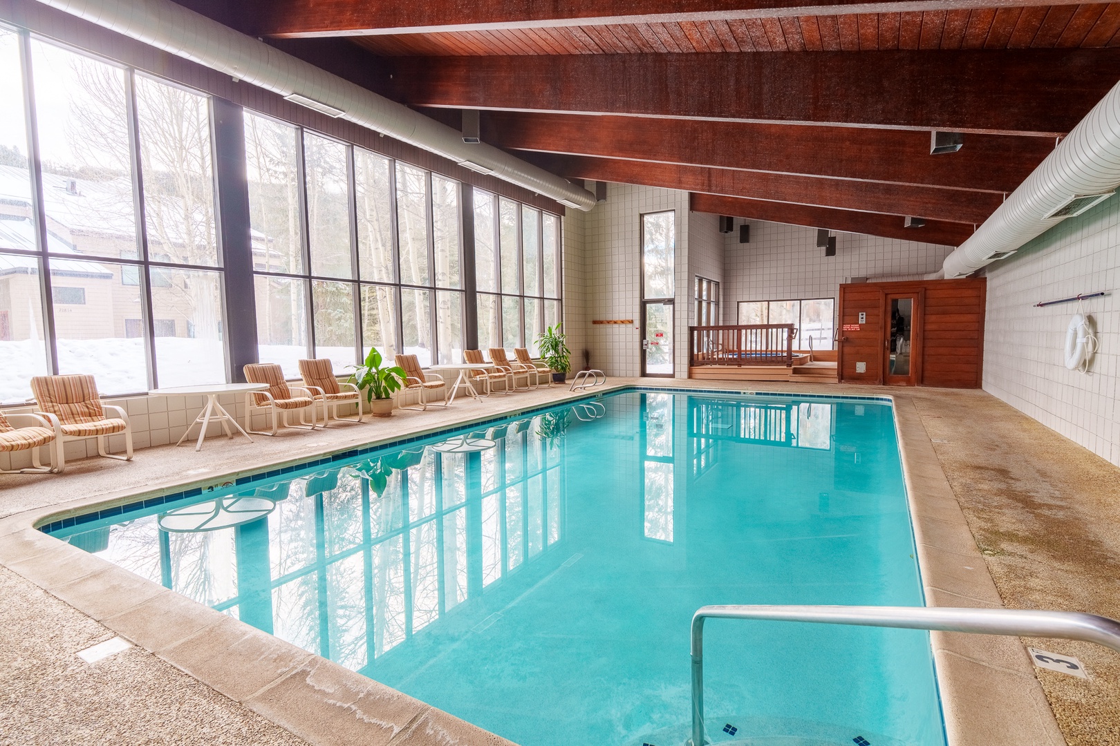 Dive into your private oasis with this stunning indoor pool, where warm wood beams and floor-to-ceiling windows create the perfect year-round swimming sanctuary.