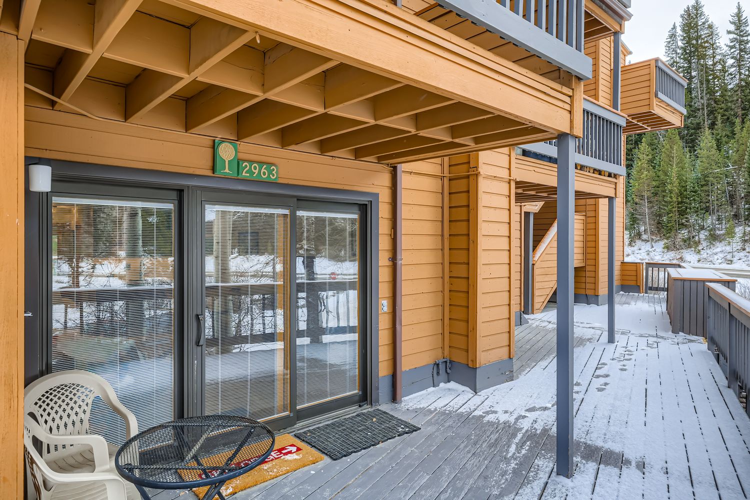 Property entrance featuring unit 2963 with a welcoming covered deck area surrounded by snowy winter scenery and evergreen forest.