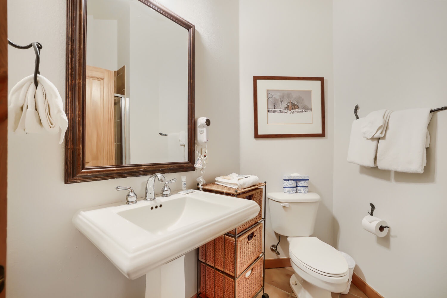 Your private bathroom features a classic pedestal sink, cozy wicker storage, and fresh towels ready for you. It's a bright, inviting space where you'll feel right at home.