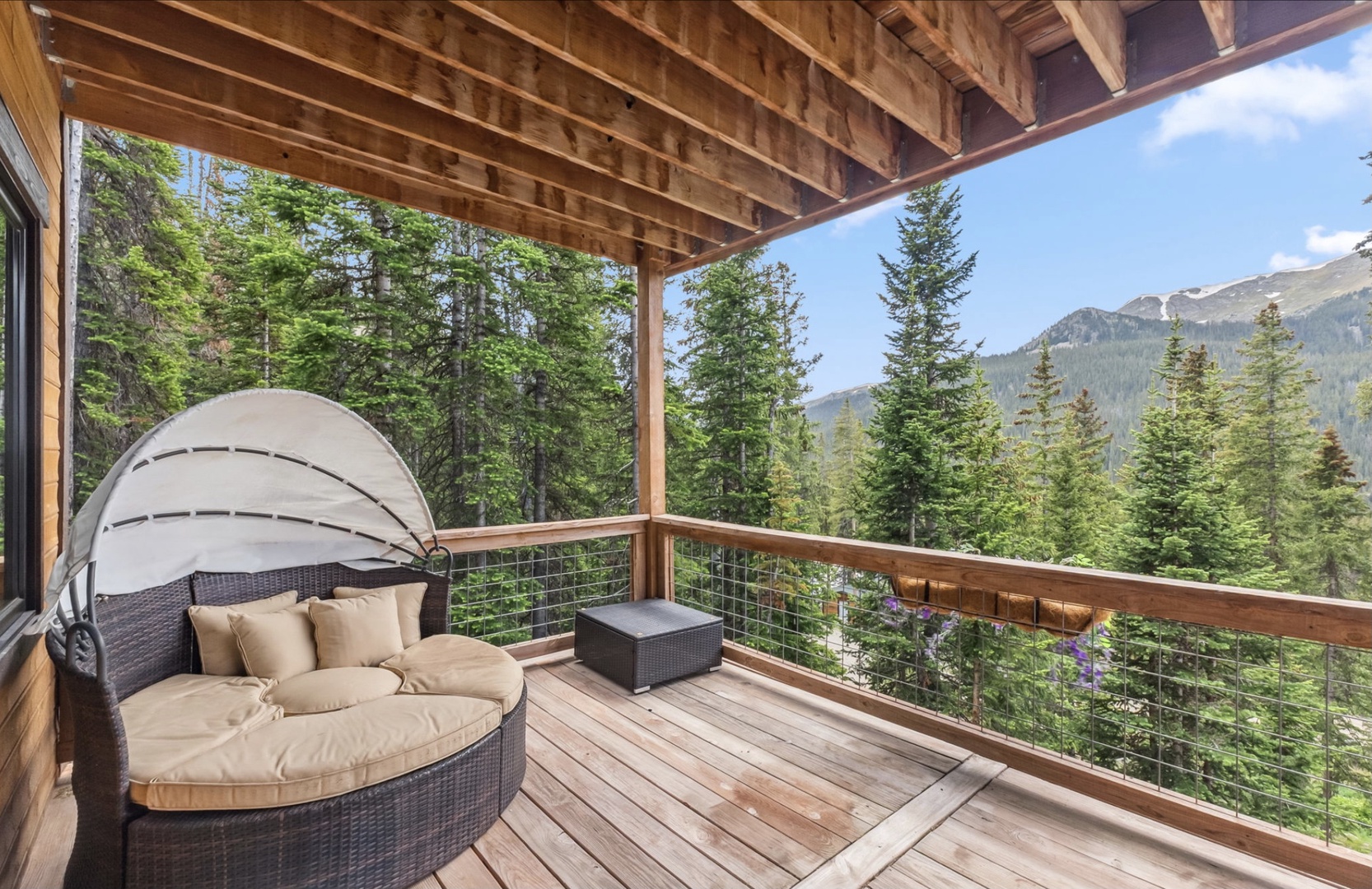 A serene covered deck with a cozy daybed invites you to unwind while taking in sweeping mountain and forest views—your peaceful retreat awaits.