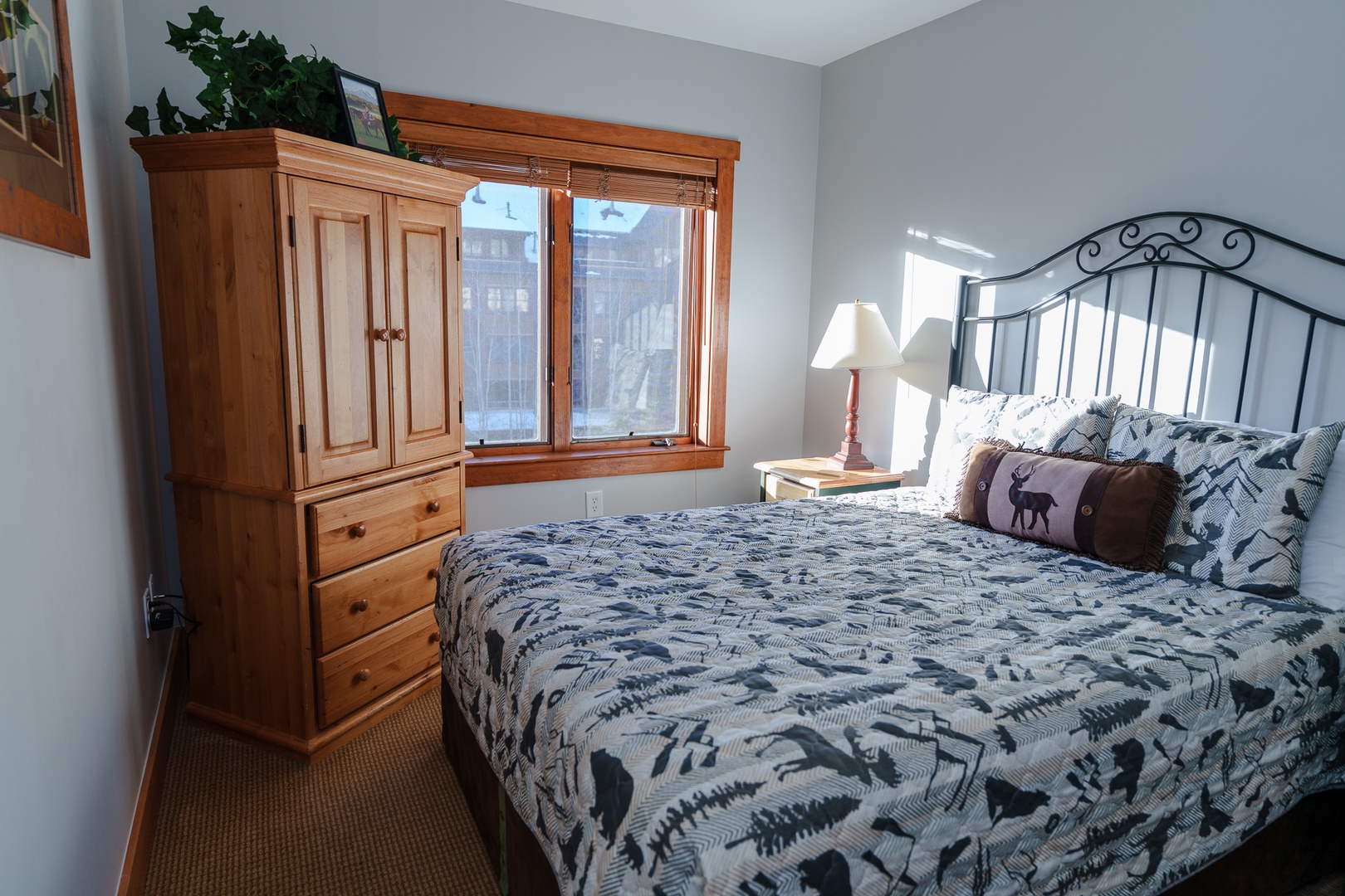 Relax in your cozy bedroom featuring a comfortable queen bed with charming wildlife-themed bedding, warm wood furnishings, and natural light from your private window.