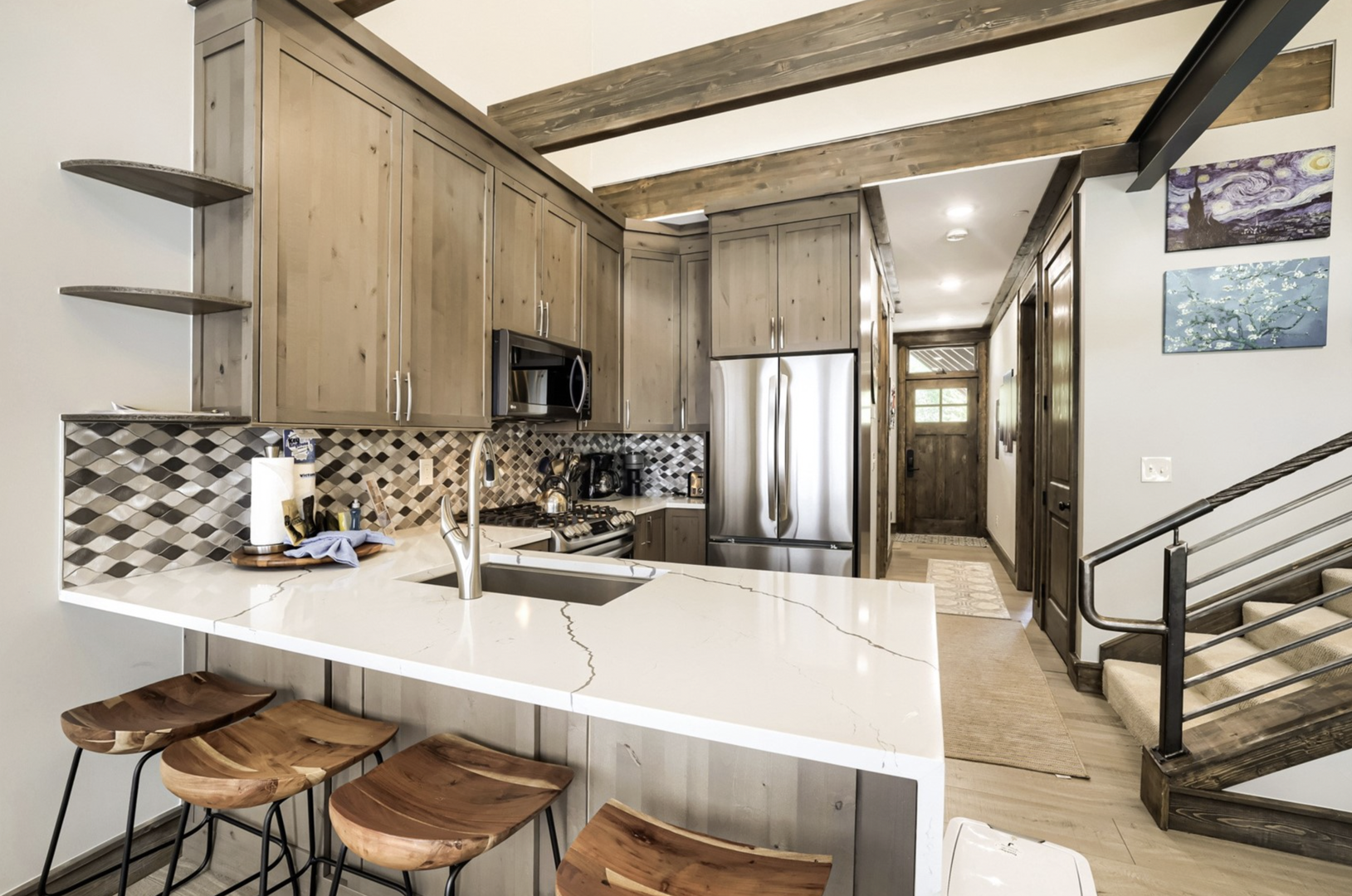 Your modern kitchen features striking marble countertops, stainless steel appliances, and a breakfast bar with rustic wooden stools—perfect for morning coffee or casual meals.
