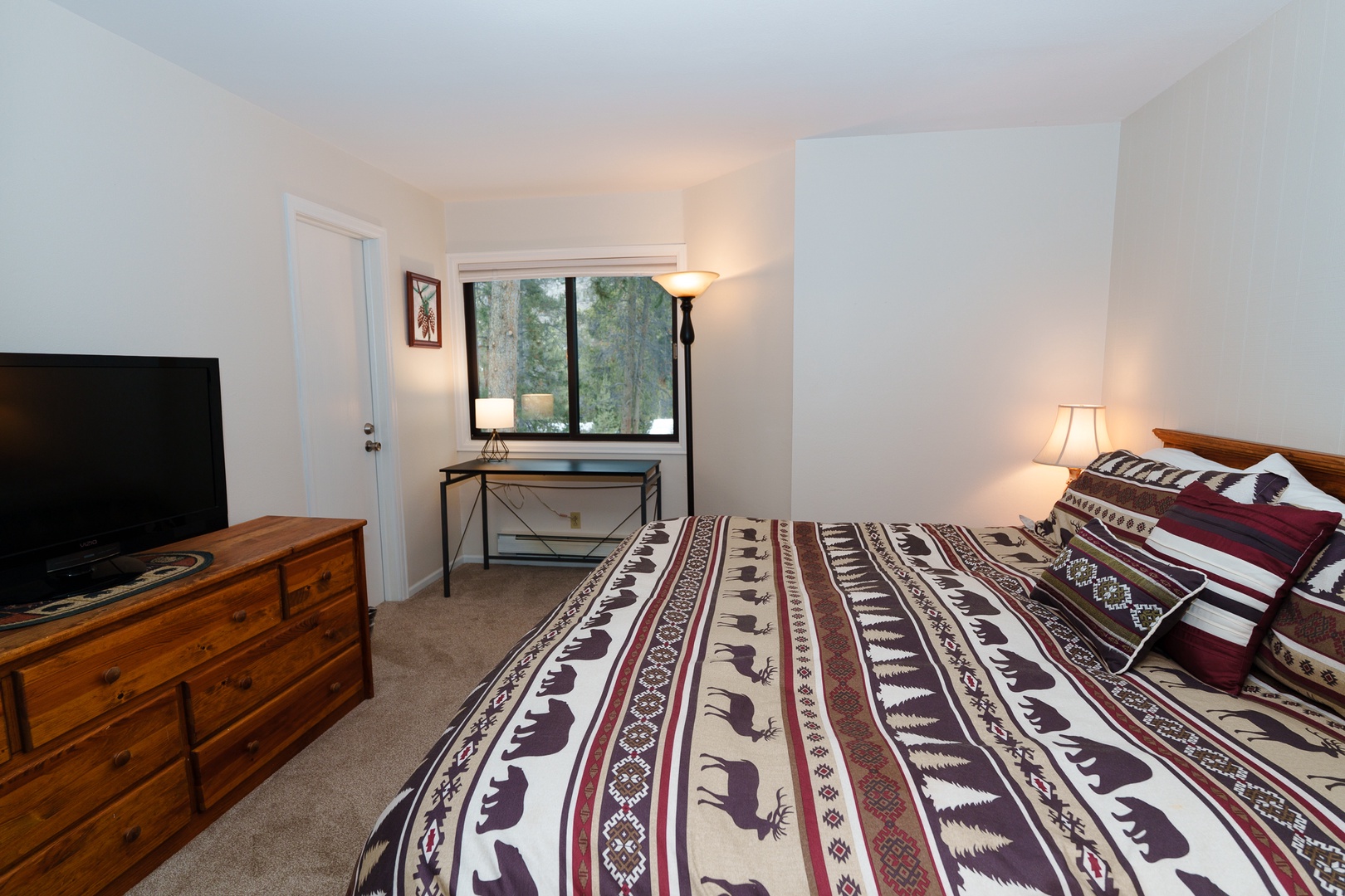 Your cozy primary bedroom features a comfortable bed with rustic wildlife-themed bedding, a TV for entertainment, and a peaceful forest view from your window.