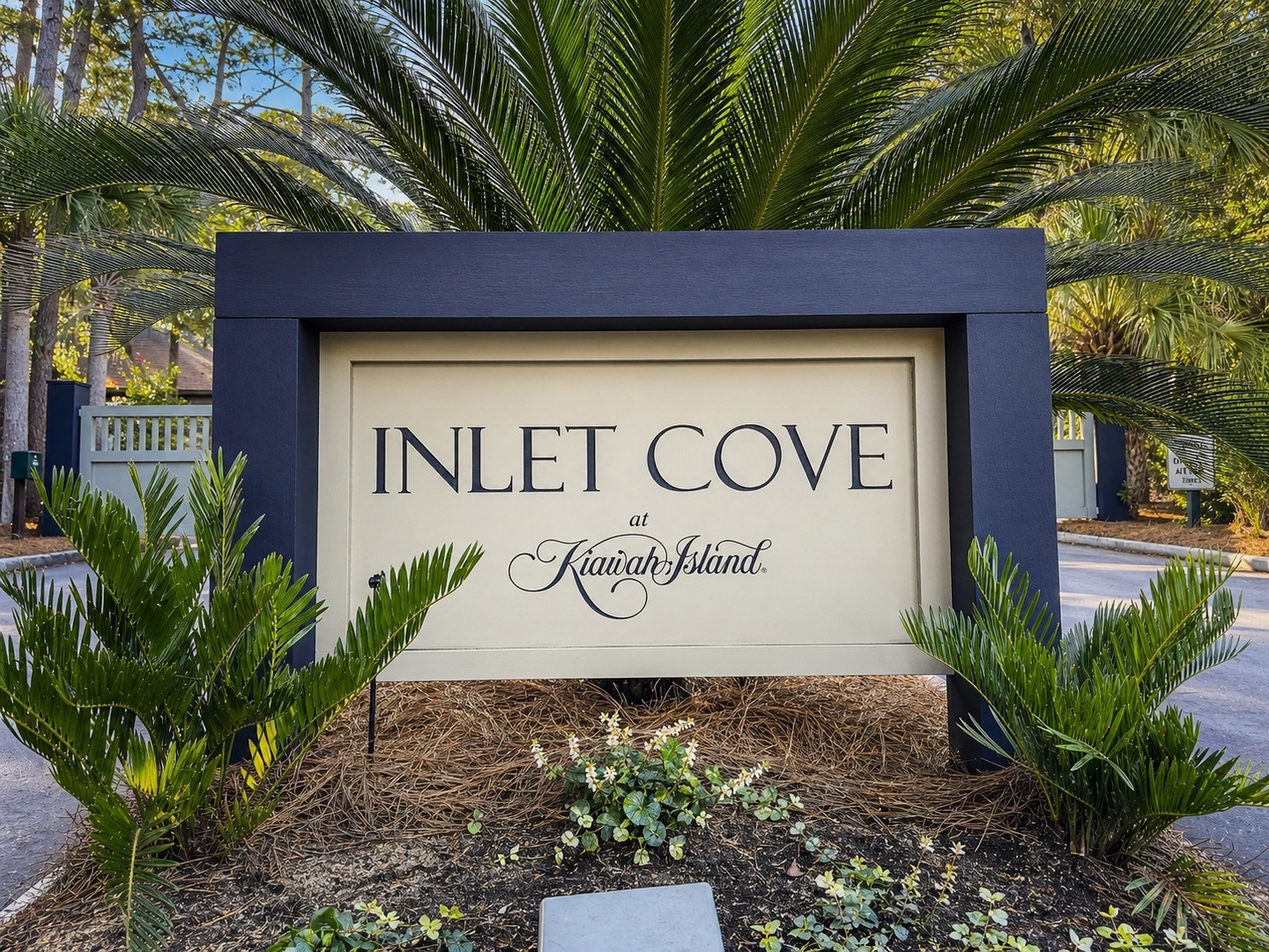 Elegant entrance marker for Inlet Cove at Kiawah Island, featuring sophisticated signage surrounded by lush tropical landscaping and mature palm trees.