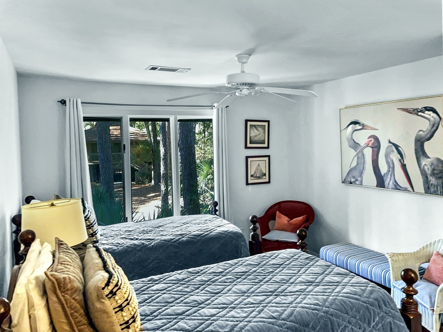 Your restful twin bedroom overlooks lush gardens, featuring coastal bird artwork and a cozy reading chair for peaceful moments.