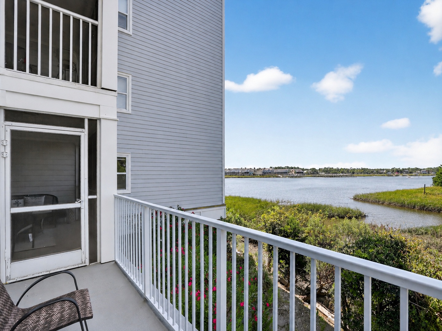Waterfront property located in a scenic community with views across the lake to neighboring homes and open sky, surrounded by green grasses and shrubs.