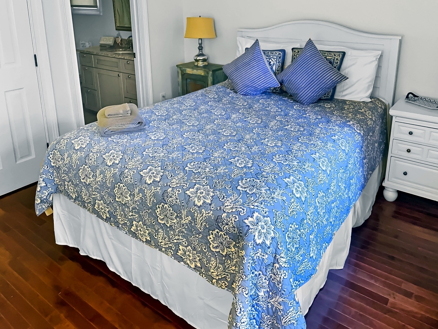 Drift off in your elegant bedroom featuring crisp linens, charming blue florals, and thoughtful touches like fresh towels.