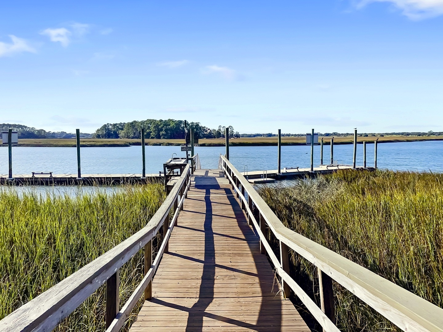 Scenic wooden dock extends over peaceful waters surrounded by salt marsh grasses and distant tree-lined shores.