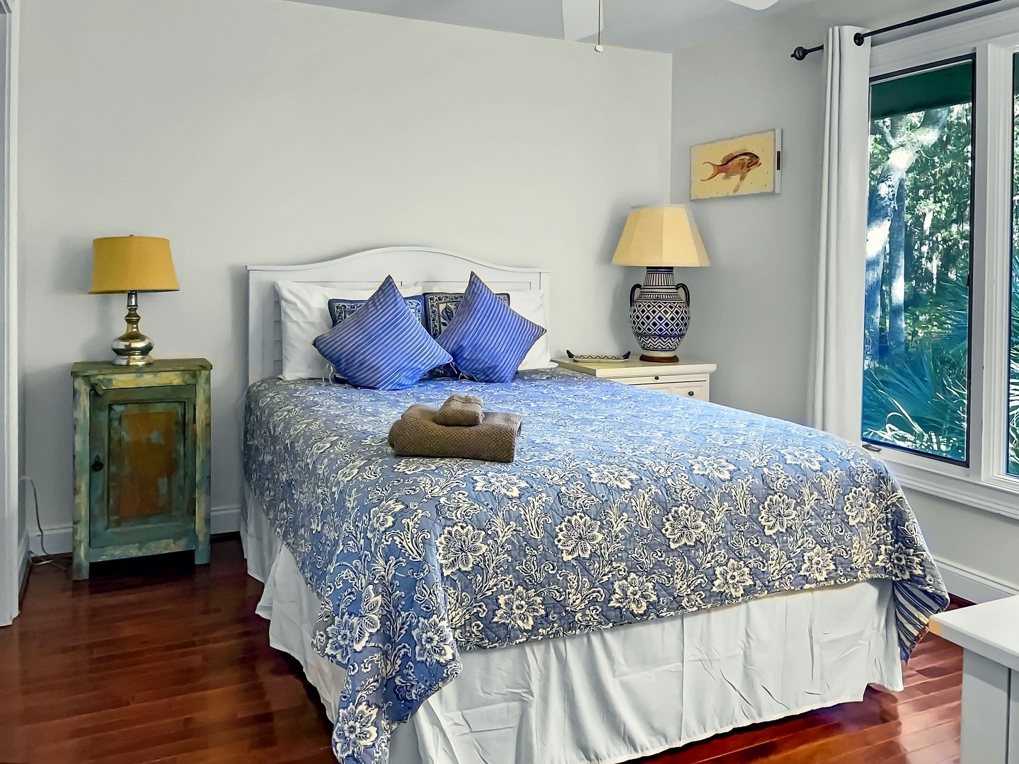 Drift off in your serene bedroom with soft blue linens and warm natural light streaming through tropical windows.