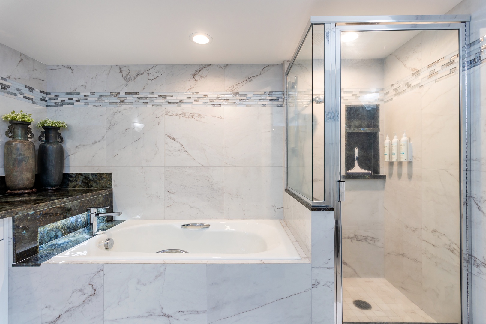 Unwind in elegant marble surroundings featuring a deep soaking tub and spacious walk-in shower with designer tile details.