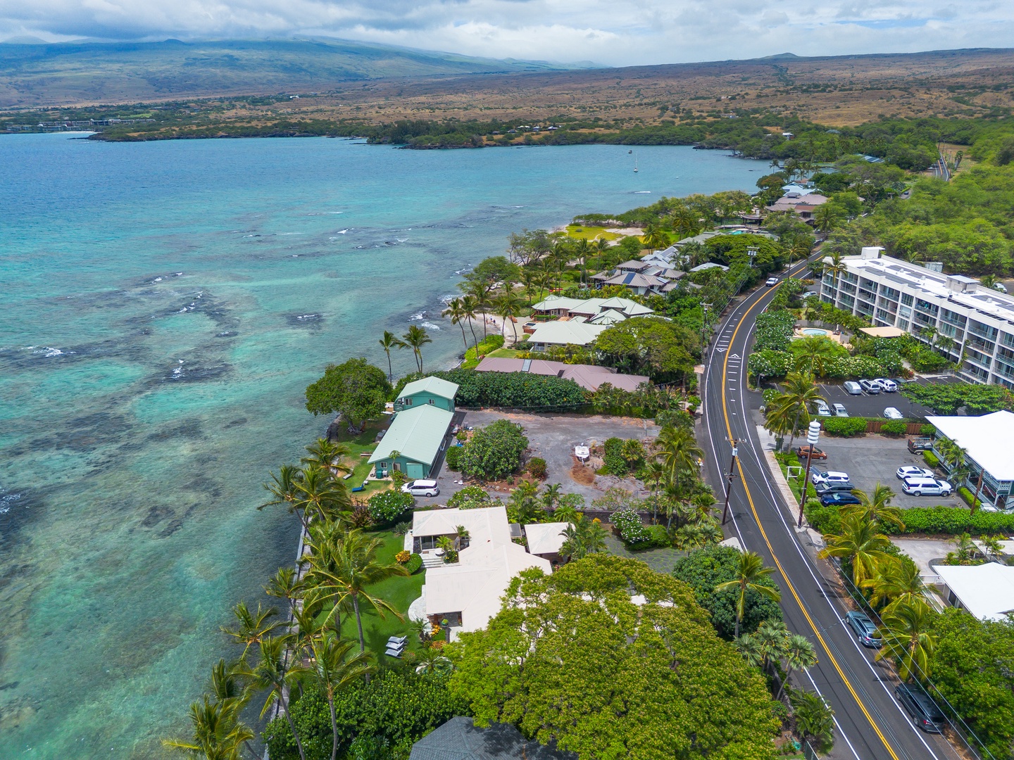 Aerial view of this Puako Beach property nestled along turquoise waters, surrounded by lush tropical landscaping and near mountain vistas.