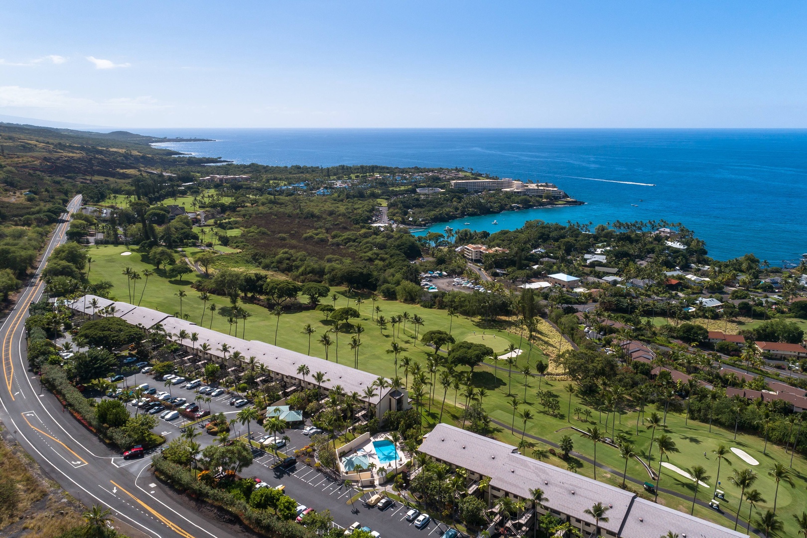 Aerial view of coastal property nestled along Hawaii's scenic shoreline, surrounded by golf greens, palm trees, and brilliant turquoise ocean waters.