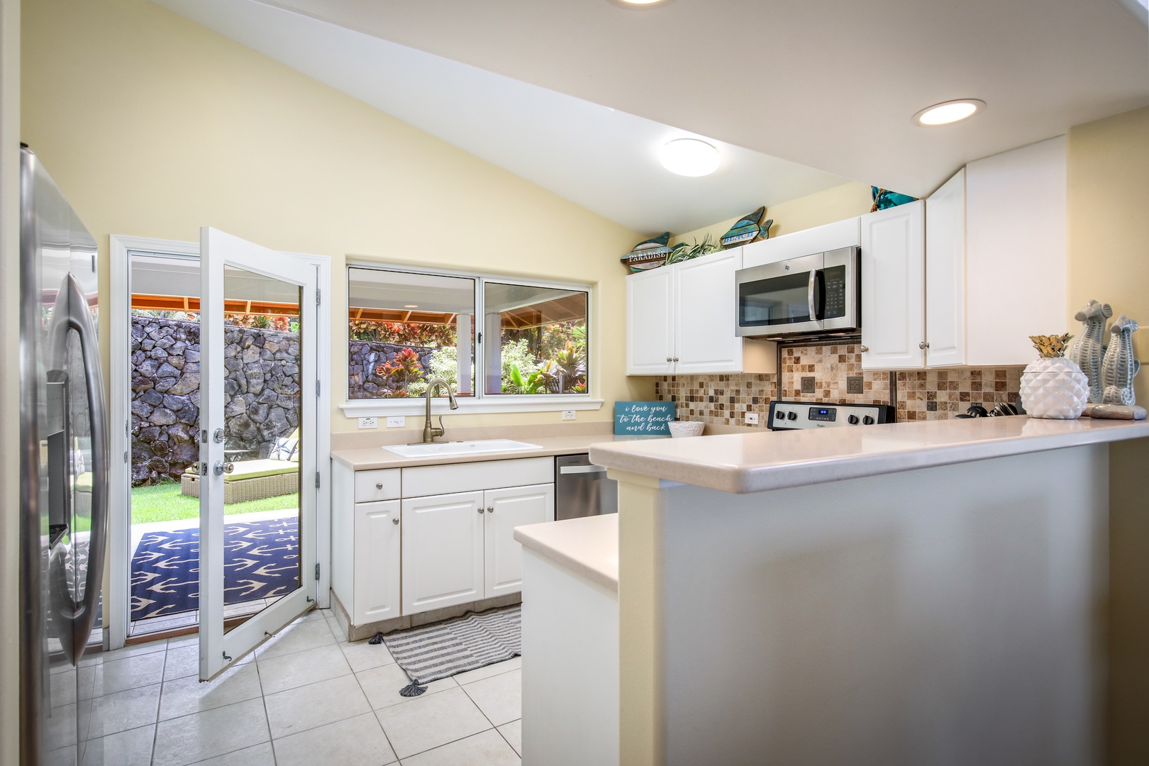 Your bright, fully-equipped kitchen awaits with modern appliances, ample counter space, and charming mosaic backsplash, opening to a peaceful backyard retreat.