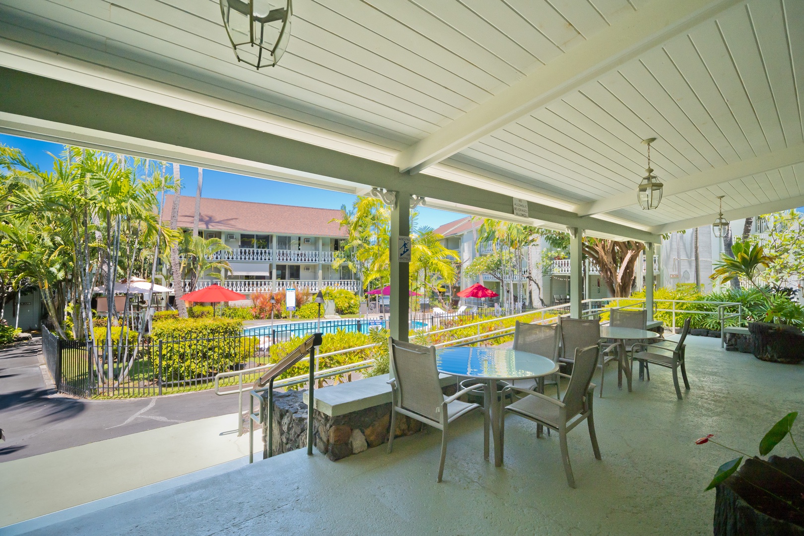 A covered outdoor seating area overlooks lush tropical landscaping and a sparkling blue pool, with lantern-style lighting creating a relaxing ambiance.