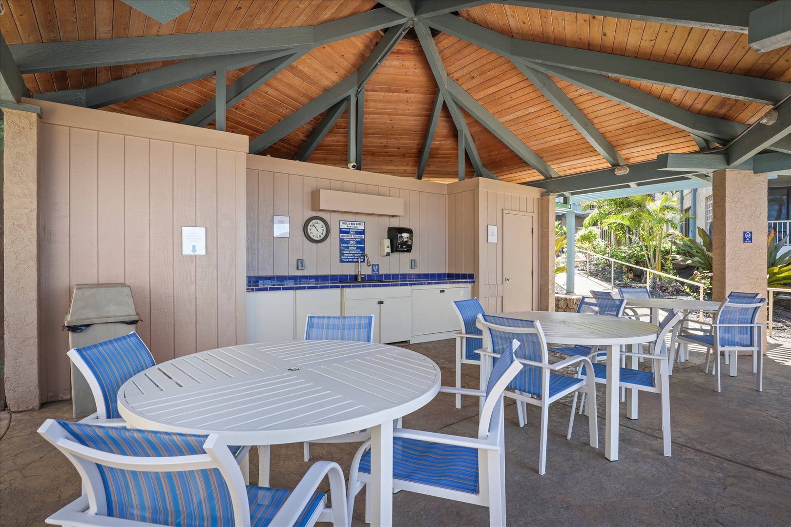A covered poolside pavilion with dining tables and BBQ facilities offers the perfect spot for your outdoor meals and gatherings, featuring shaded seating and convenient amenities under beautiful timber beams.