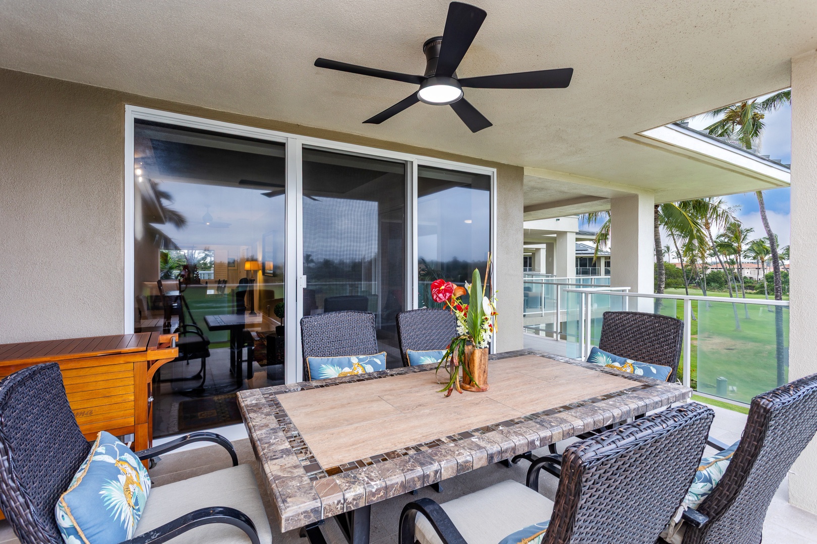 Your private balcony offers peaceful outdoor dining surrounded by lush tropical palms and tranquil pool views—perfect for morning coffee or evening meals under the ceiling fan's gentle breeze.